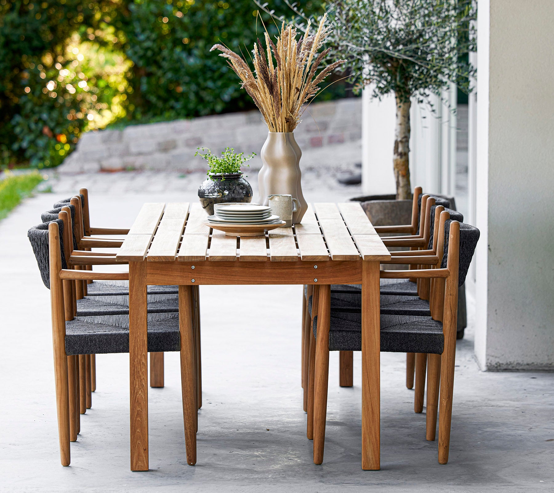 Una mesa de madera rodeada de ocho sillas elegantes, adornada con un jarrón y vegetación, creando un espacio de comedor acogedor.