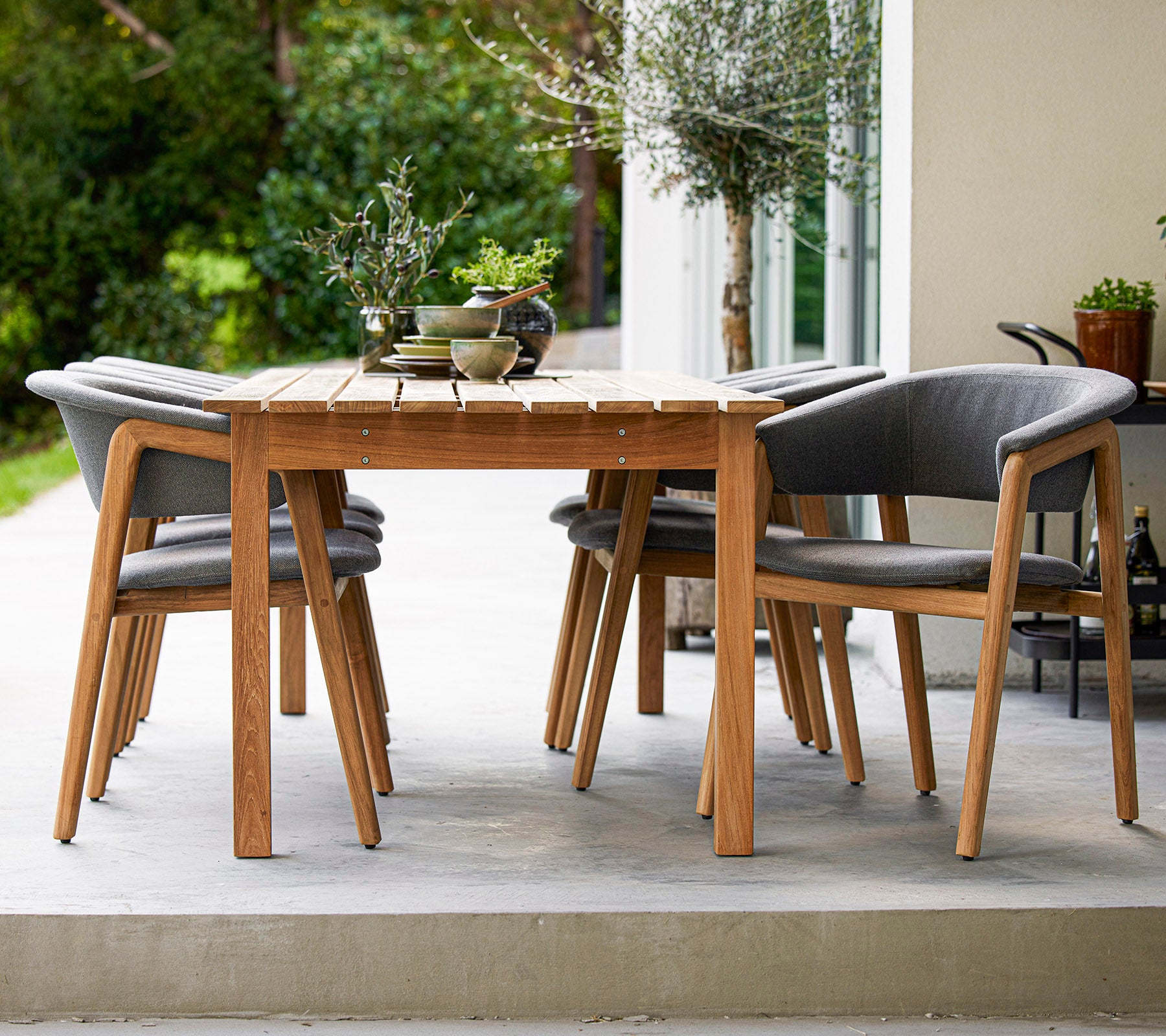 Una elegante mesa de comedor de madera rodeada de cuatro sillas acolchadas grises, perfecta para reuniones al aire libre.