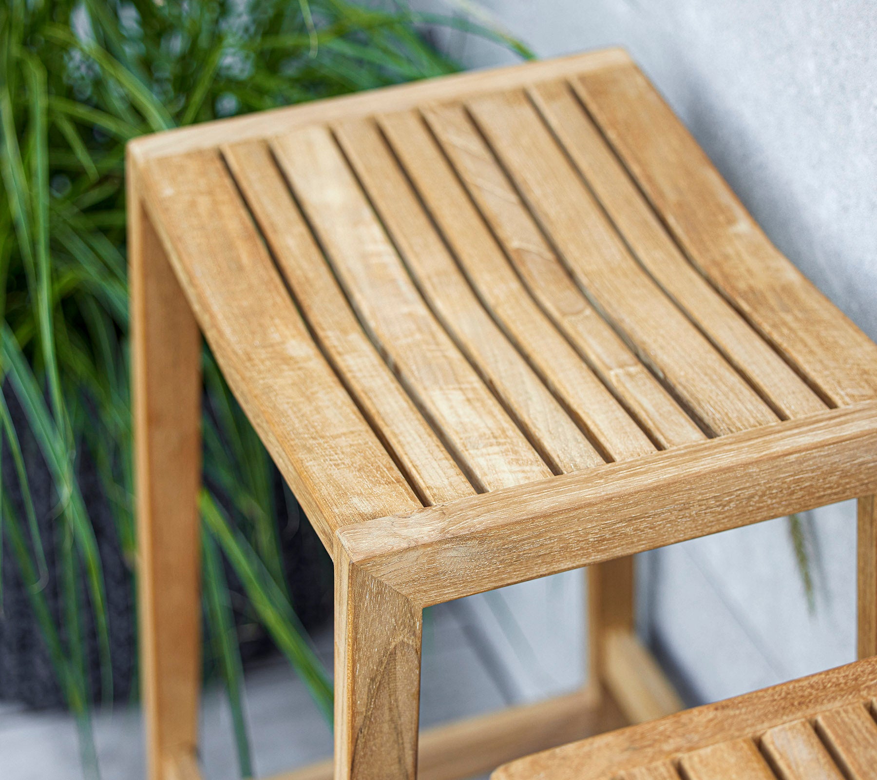 Una elegante mesa auxiliar de madera con diseño de tapa de listones, con un acabado claro que complementa la vegetación circundante.