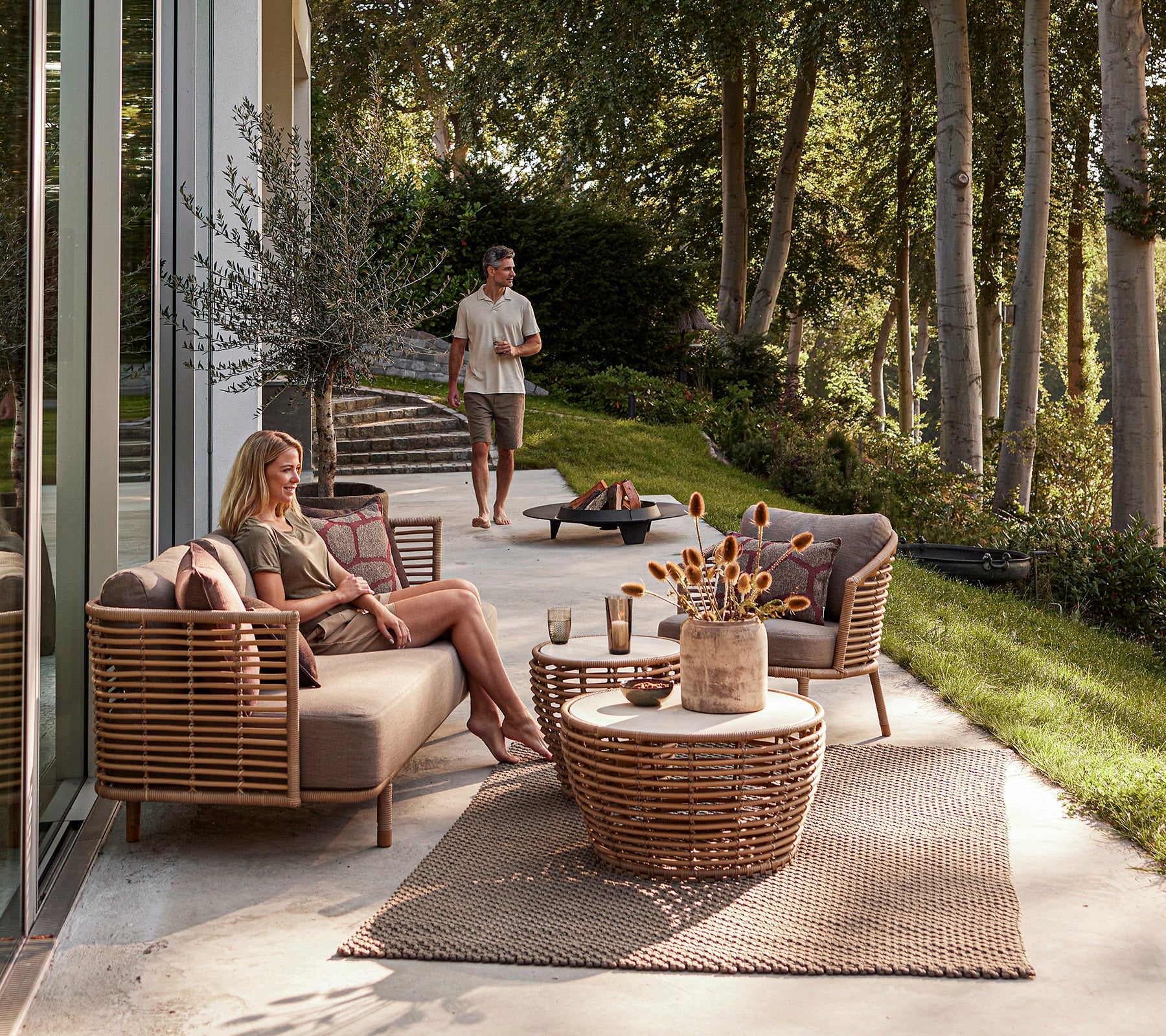 Una elegante área de descanso al aire libre con muebles tejidos, una mesa de café decorativa y un ambiente relajado con vegetación de fondo.