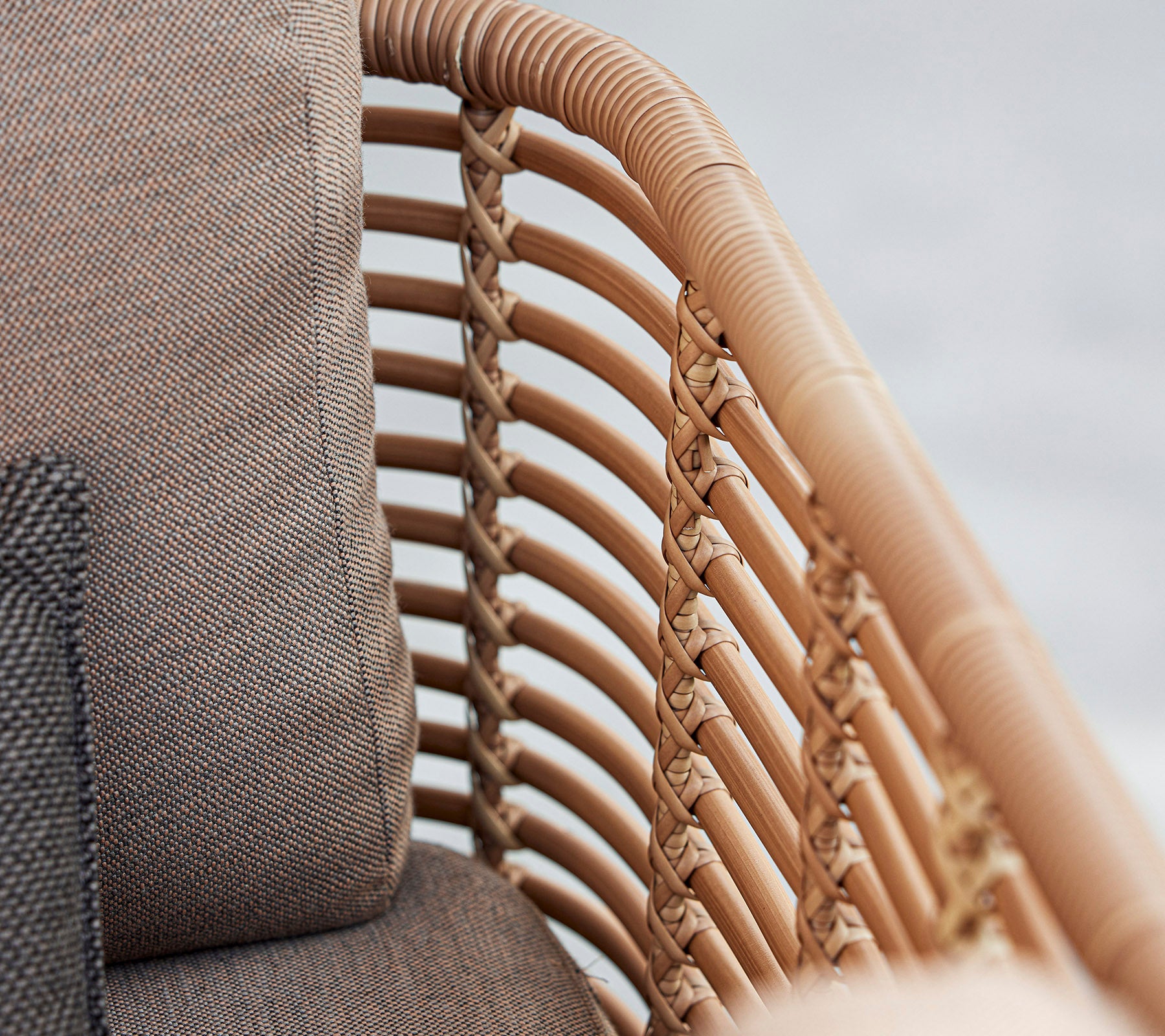 Acercamiento a una silla elegante con detalles de ratán trenzado y suaves cojines en tonos neutros, que muestran un diseño moderno.