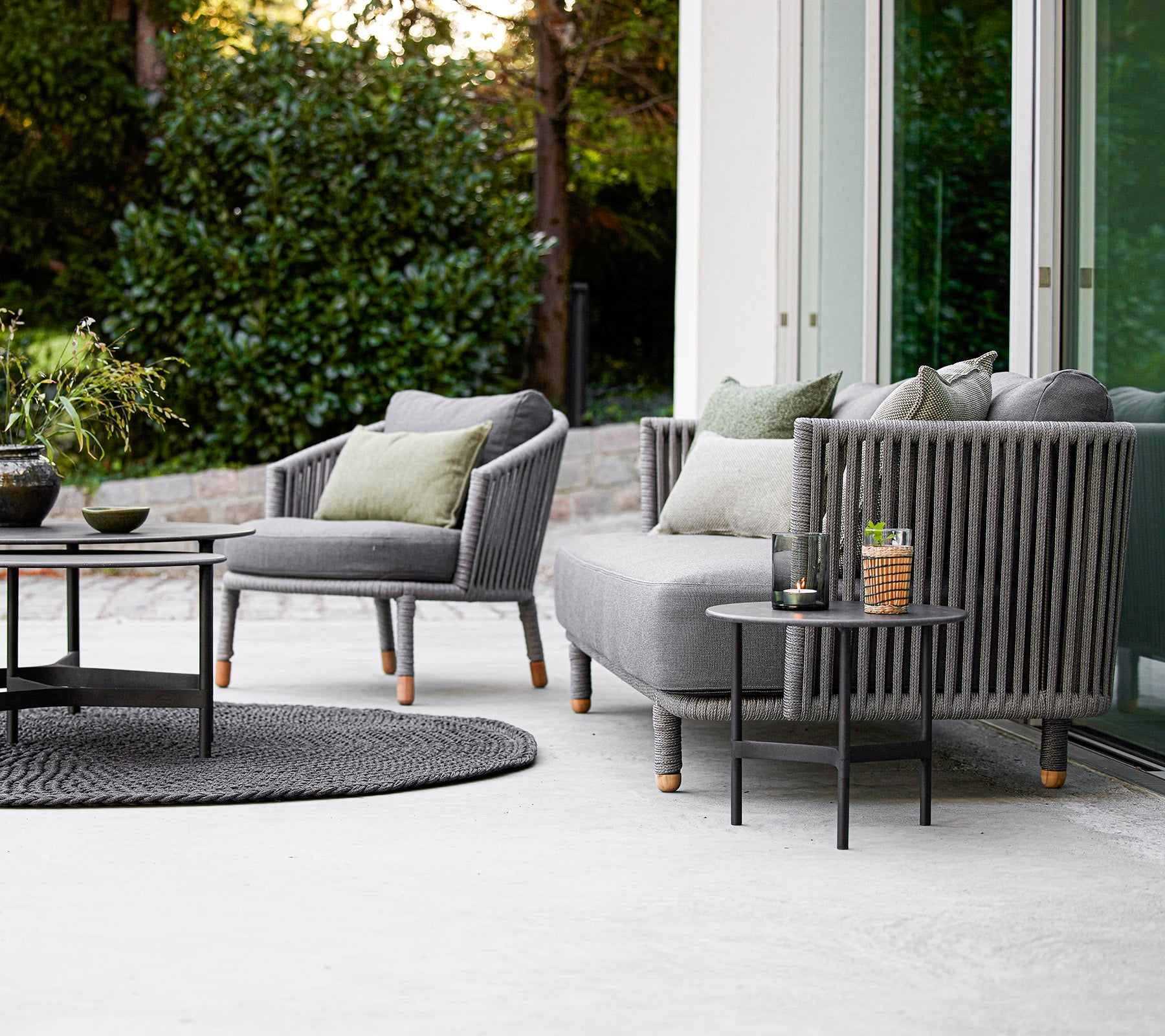 Conjunto de muebles de exterior contemporáneo que incluye un sofá y sillones con cojines, acompañado de una mesa de café redonda y accesorios decorativos.