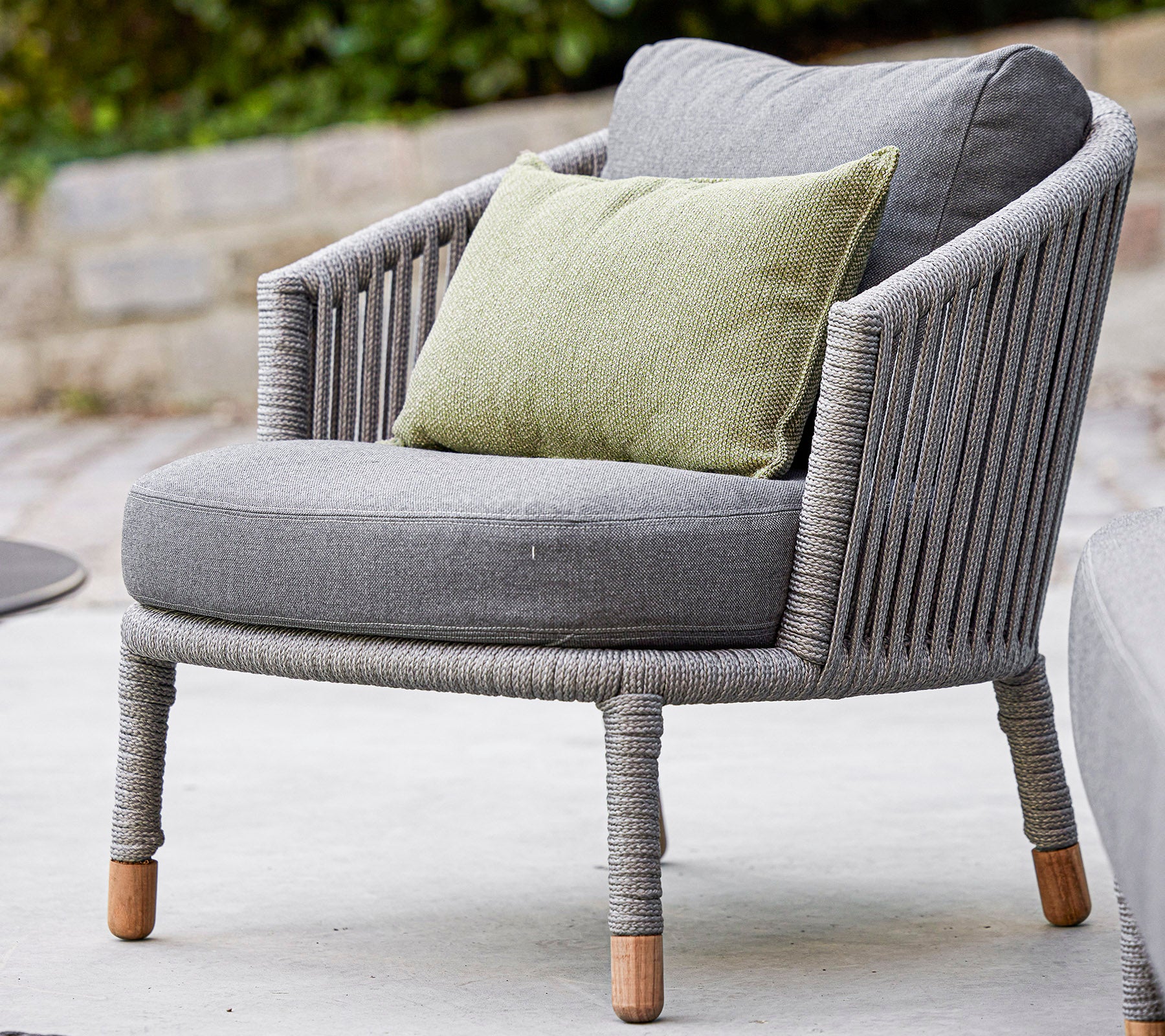 Silla gris elegante con un diseño redondeado y un acogedor cojín verde, con tela texturizada y patas de madera natural. Perfecta para relajarse.