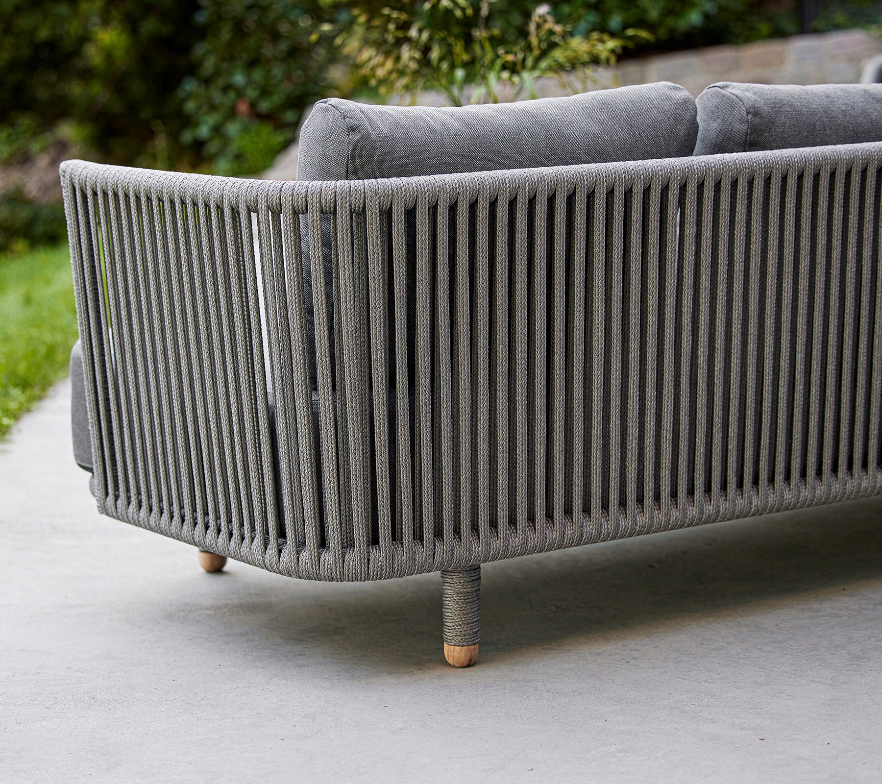 Sofá gris elegante y moderno con diseño de lamas verticales y patas de madera, ideal para espacios exteriores o de estar contemporáneos.