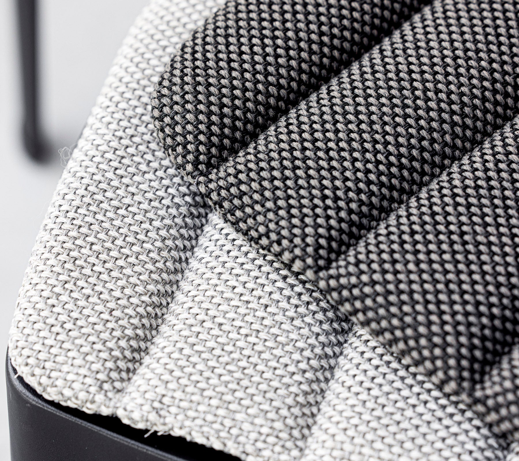 Primer plano de un asiento de tela texturizada, que muestra una mezcla de patrones tejidos en gris claro y oscuro con un diseño moderno. Ideal para interiores contemporáneos.