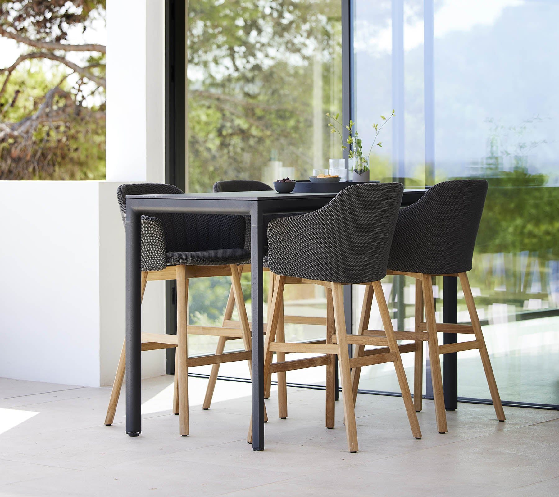 Una mesa de bar elegante acompañada de cuatro modernas sillas de bar con patas de madera y asientos tapizados.