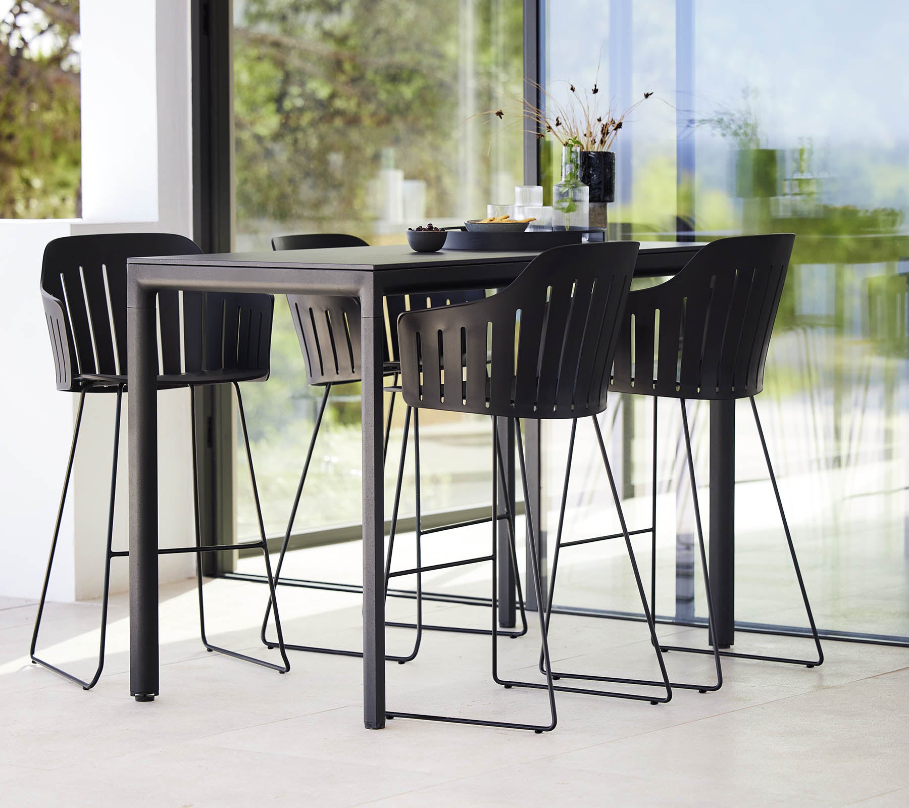 Una elegante mesa de bar negra acompañada de modernas sillas de bar con un diseño de listones, creando una disposición de asientos con estilo.