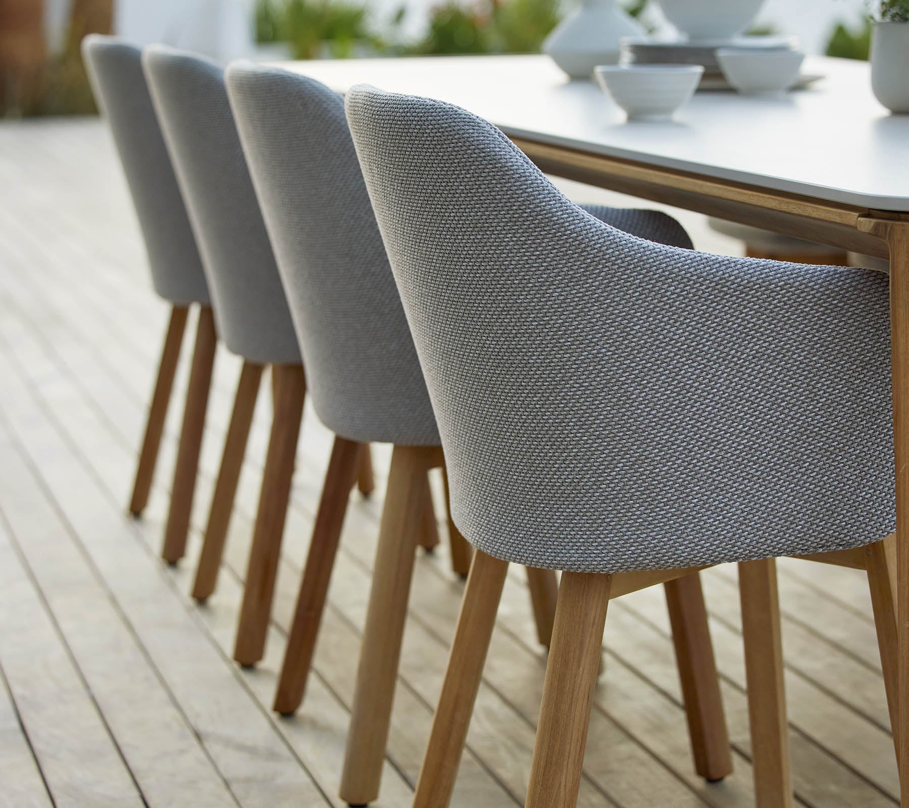 Una fila de sillas modernas tapizadas con patas de madera dispuestas ordenadamente al lado de una mesa, que muestra un diseño elegante y contemporáneo.