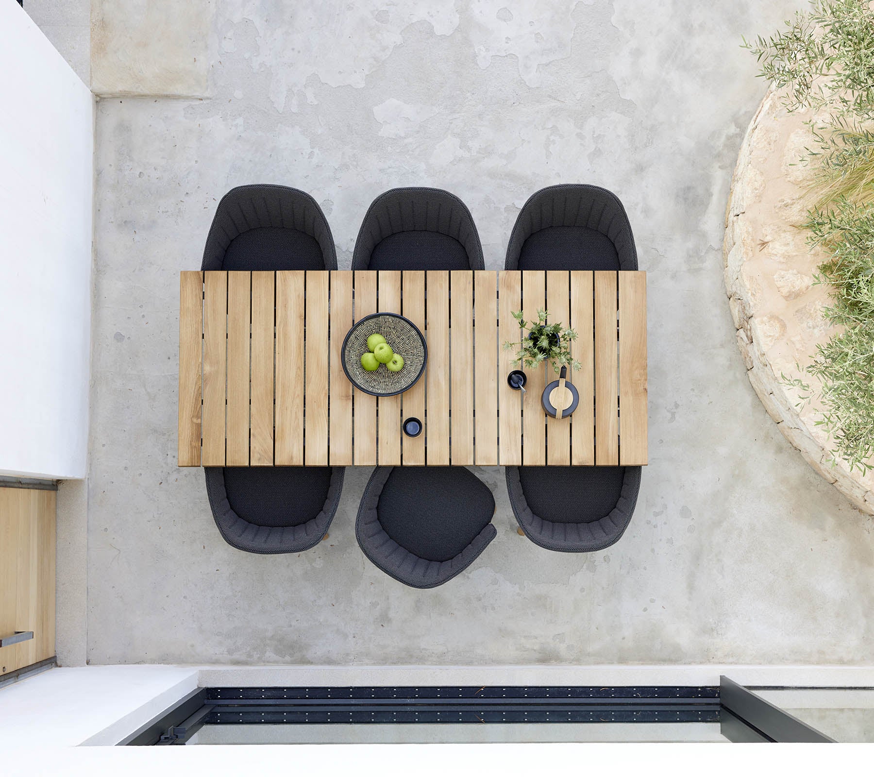 Mesa de comedor de madera elegante acompañada de cuatro sillas negras, con un tazón de fruta verde y plantas decorativas para un toque moderno.
