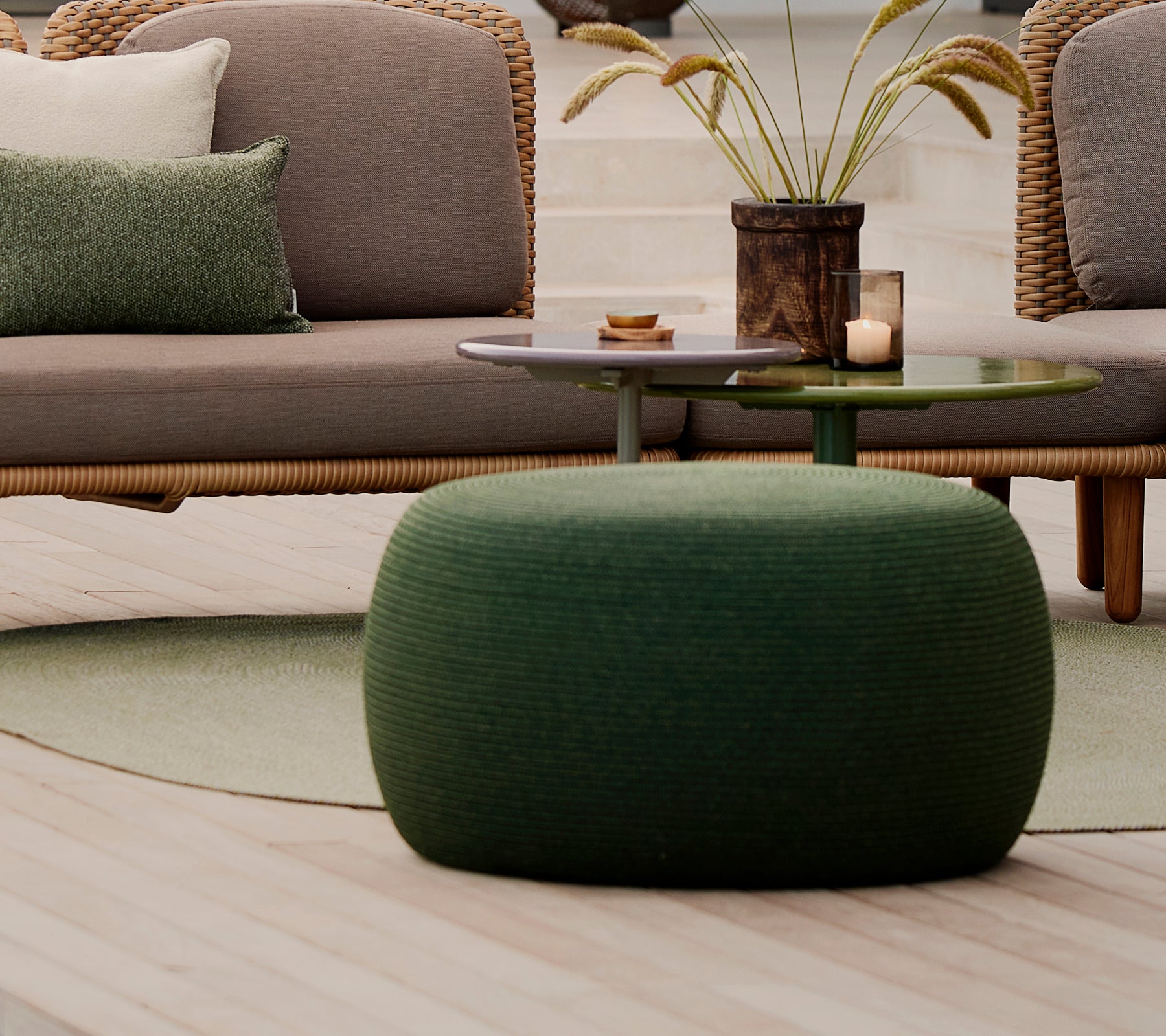 Gran otomana circular verde con una superficie texturizada, acompañada de una mesa pequeña y elementos decorativos.