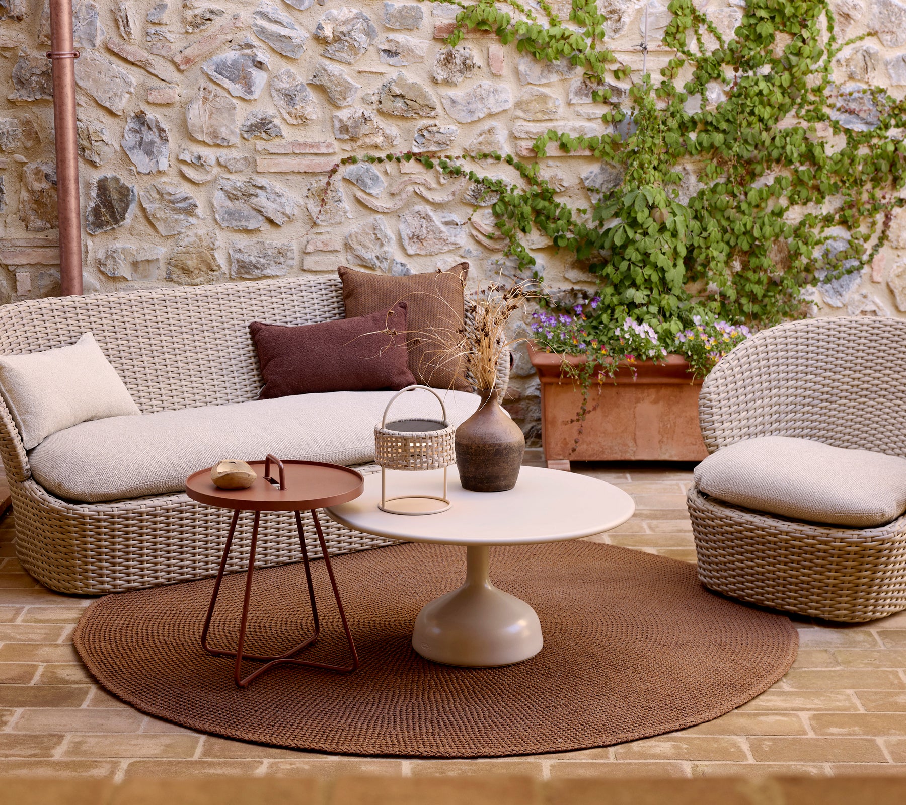 Área de estar acogedora con una alfombra de punto, una mesa de café brillante y una mesa auxiliar elegante, acentuada con cojines decorativos y vegetación.