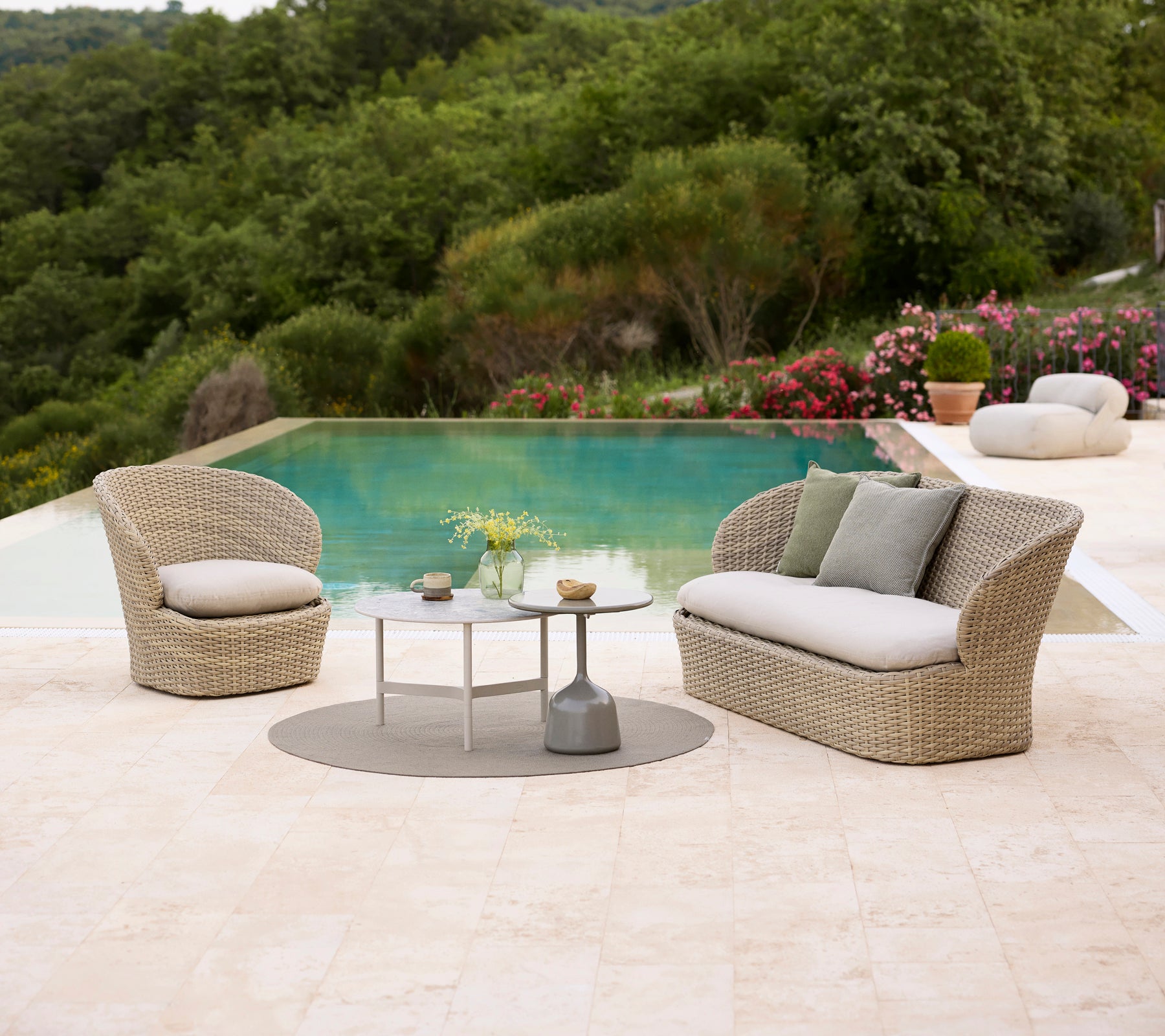 Muebles de lounge costero con cojines suaves, combinados con una mesa de café Twist y una mesa de café Glaze, rodeados de una abundante vegetación y una piscina.