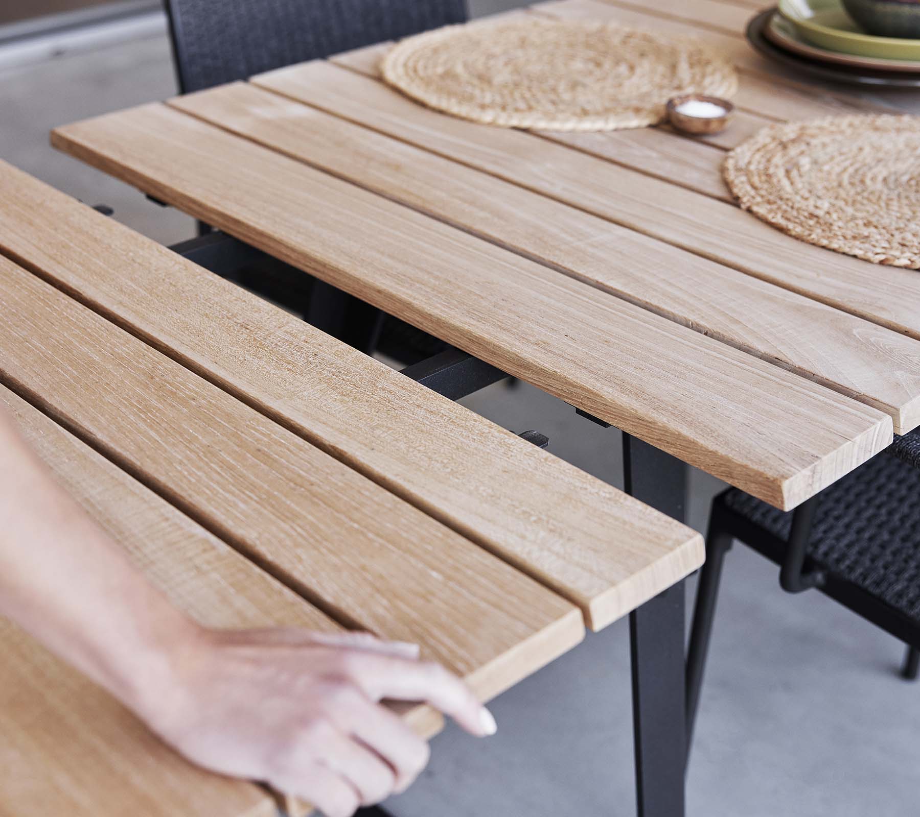 Detalle de una mesa de madera con diseño de listones, manteles individuales y una estética minimalista, perfecta para cenar o reuniones.