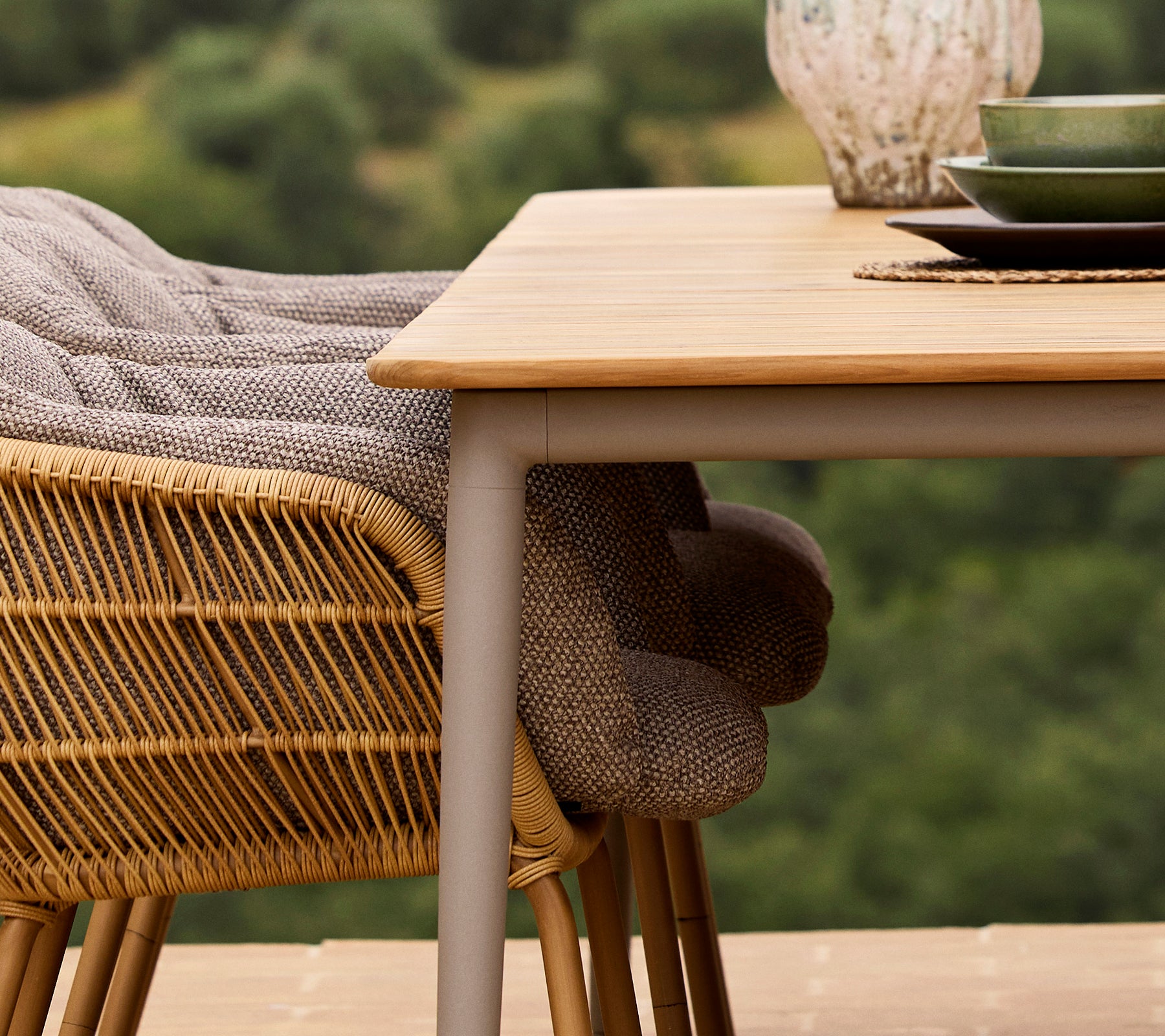 Primer plano de una mesa de comedor Core con una silla Stay, con tejido entrelazado y un plato verde frente a un fondo natural.