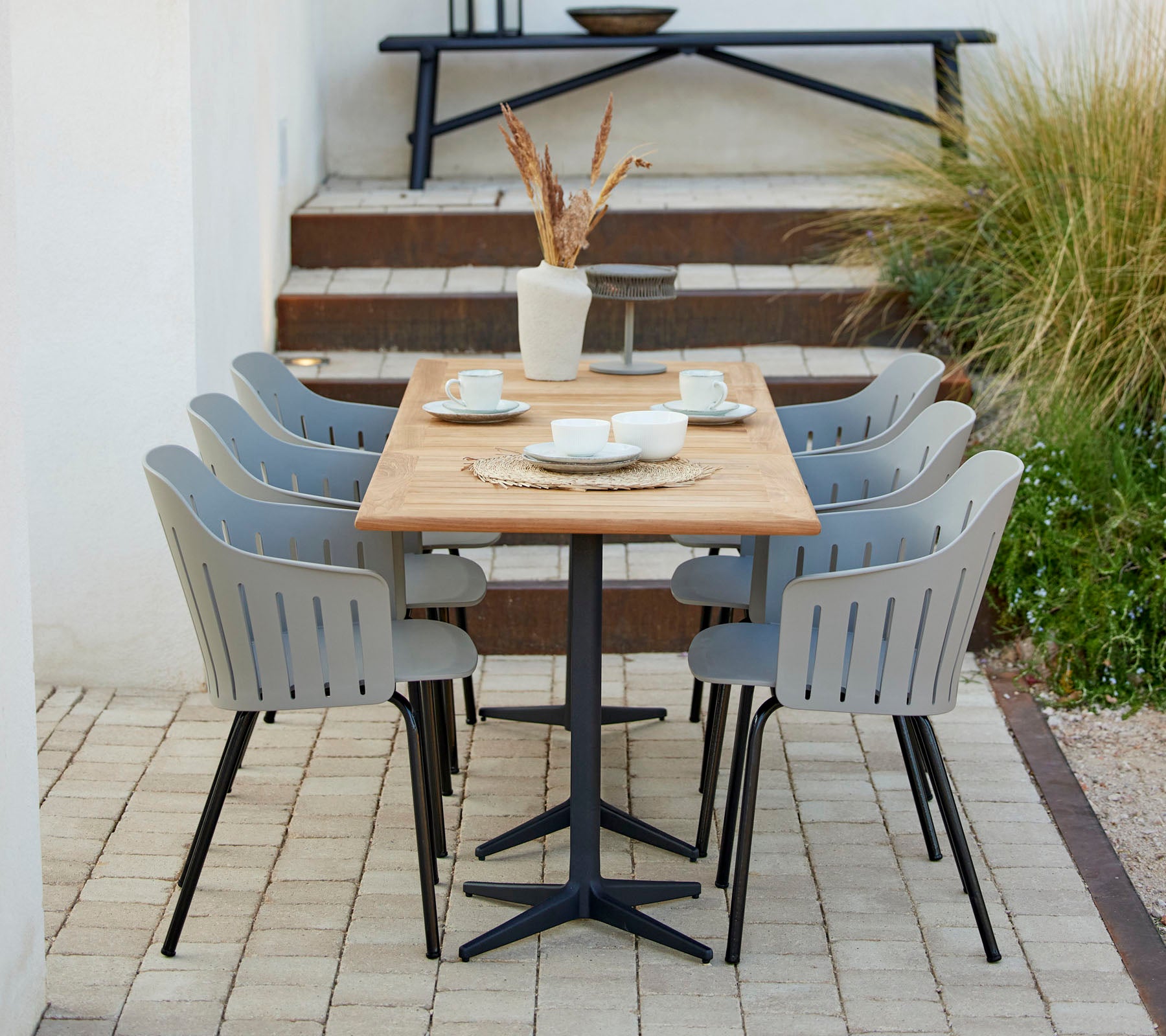 Una elegante configuración de comedor con una mesa de madera rodeada de sillas grises, complementada con objetos decorativos y vegetación.