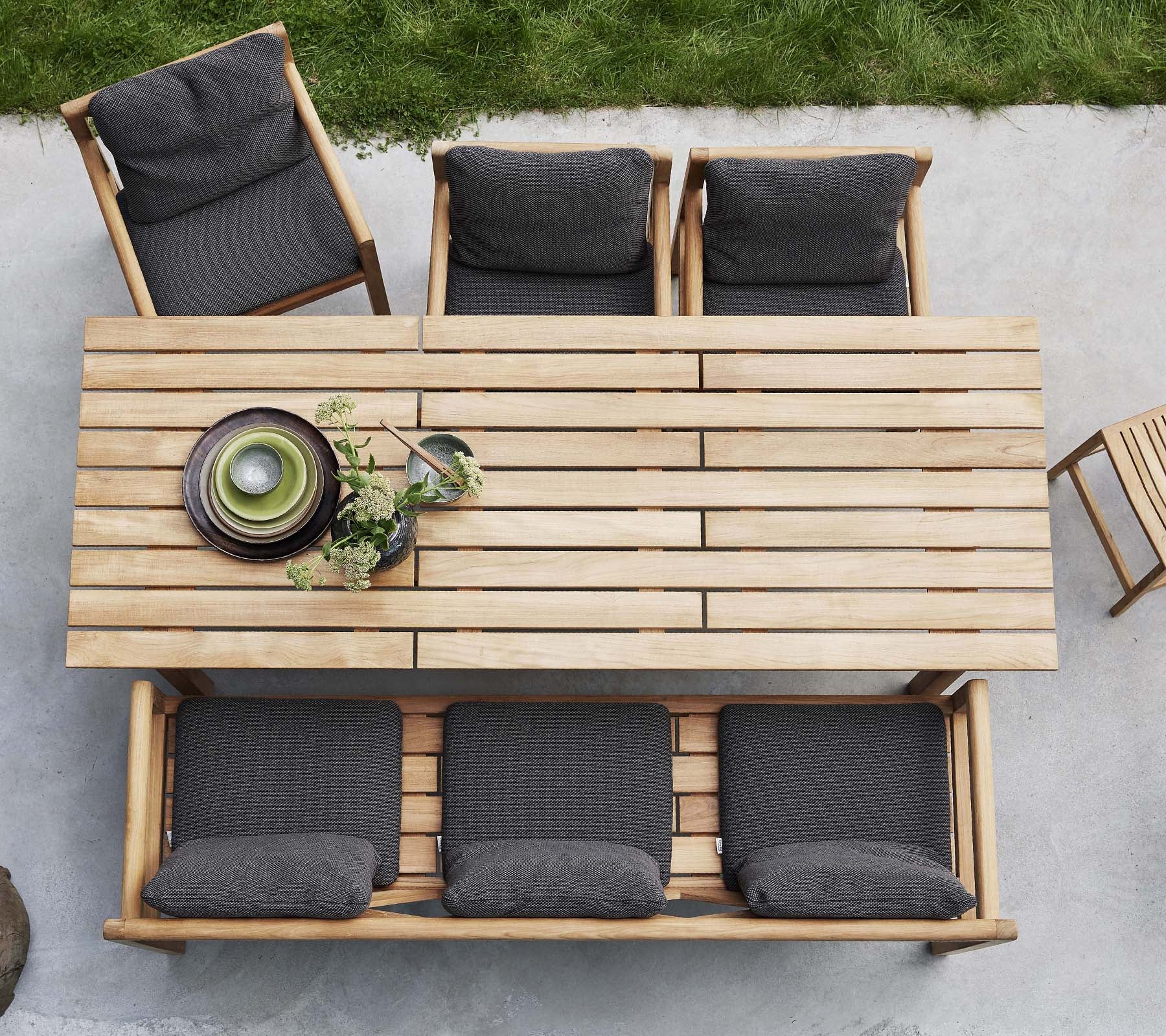 Una mesa de madera acompañada de cuatro sillas, cada una con cojines oscuros, con platos decorativos y vegetación sobre la mesa.