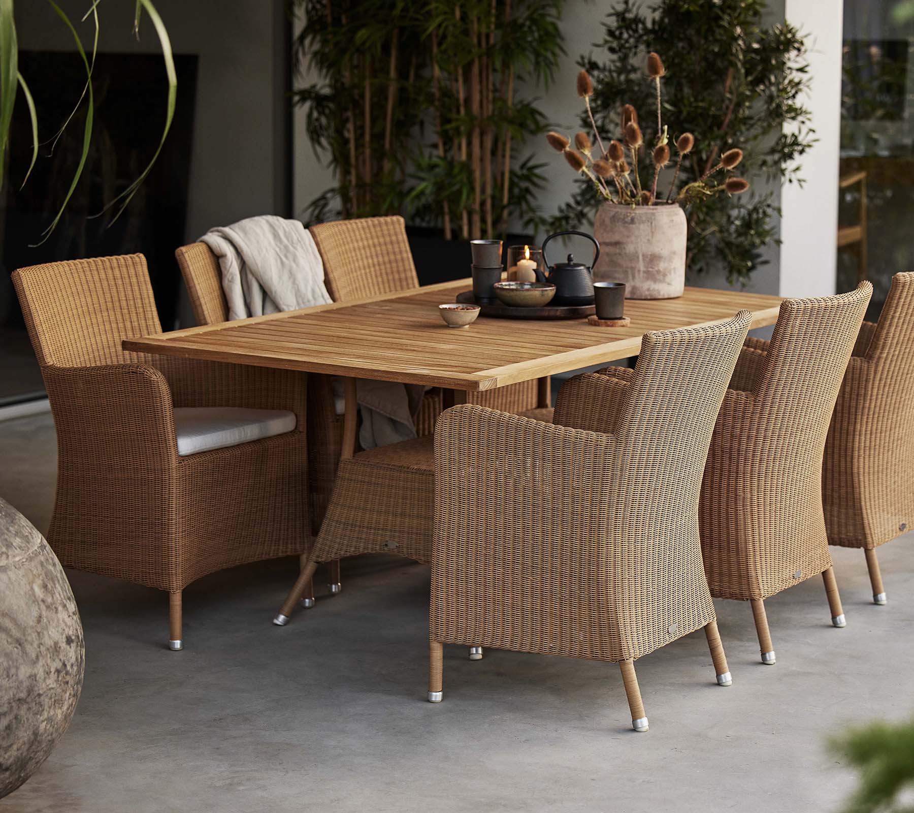Una configuración de comedor con una mesa de madera rústica rodeada de sillas Hampsted tejidas, complementada con plantas decorativas.