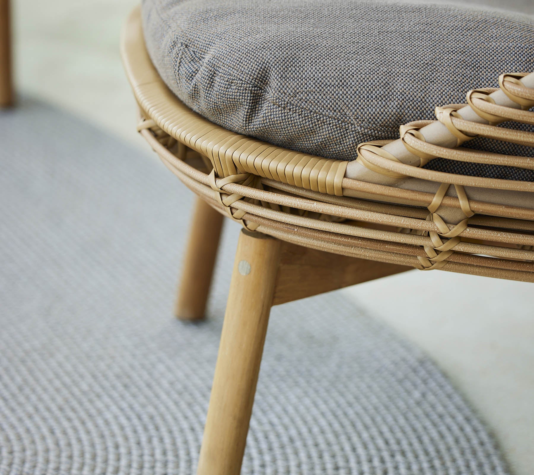 Una vista en primer plano de una silla lounge elegante con un marco tejido y un asiento acolchado, complementada con una alfombra texturizada debajo.