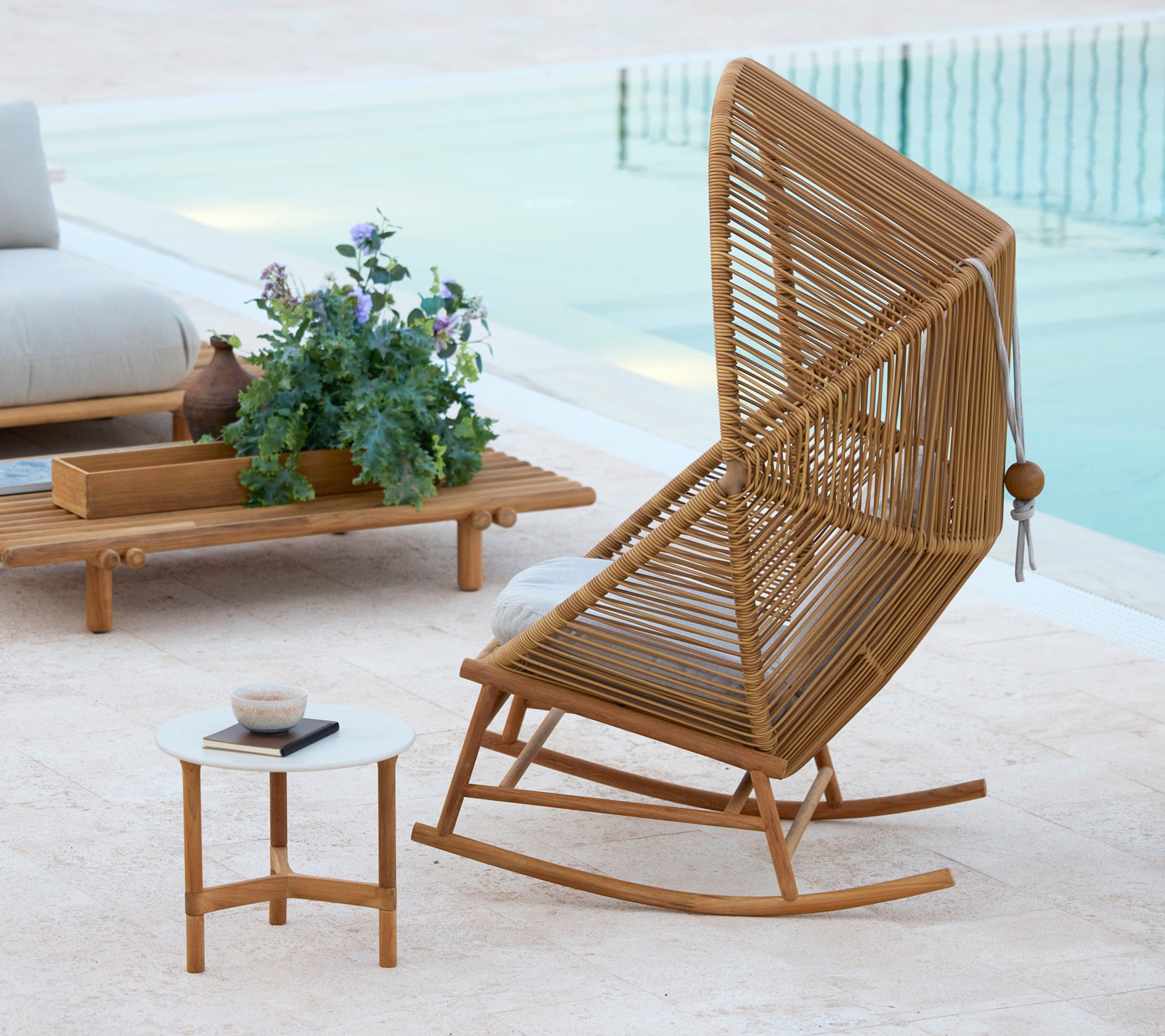 Una silla mecedora Hive elegante junto a una mesa de café Twist y una mesa de café Sticks, complementada por una planta en maceta.