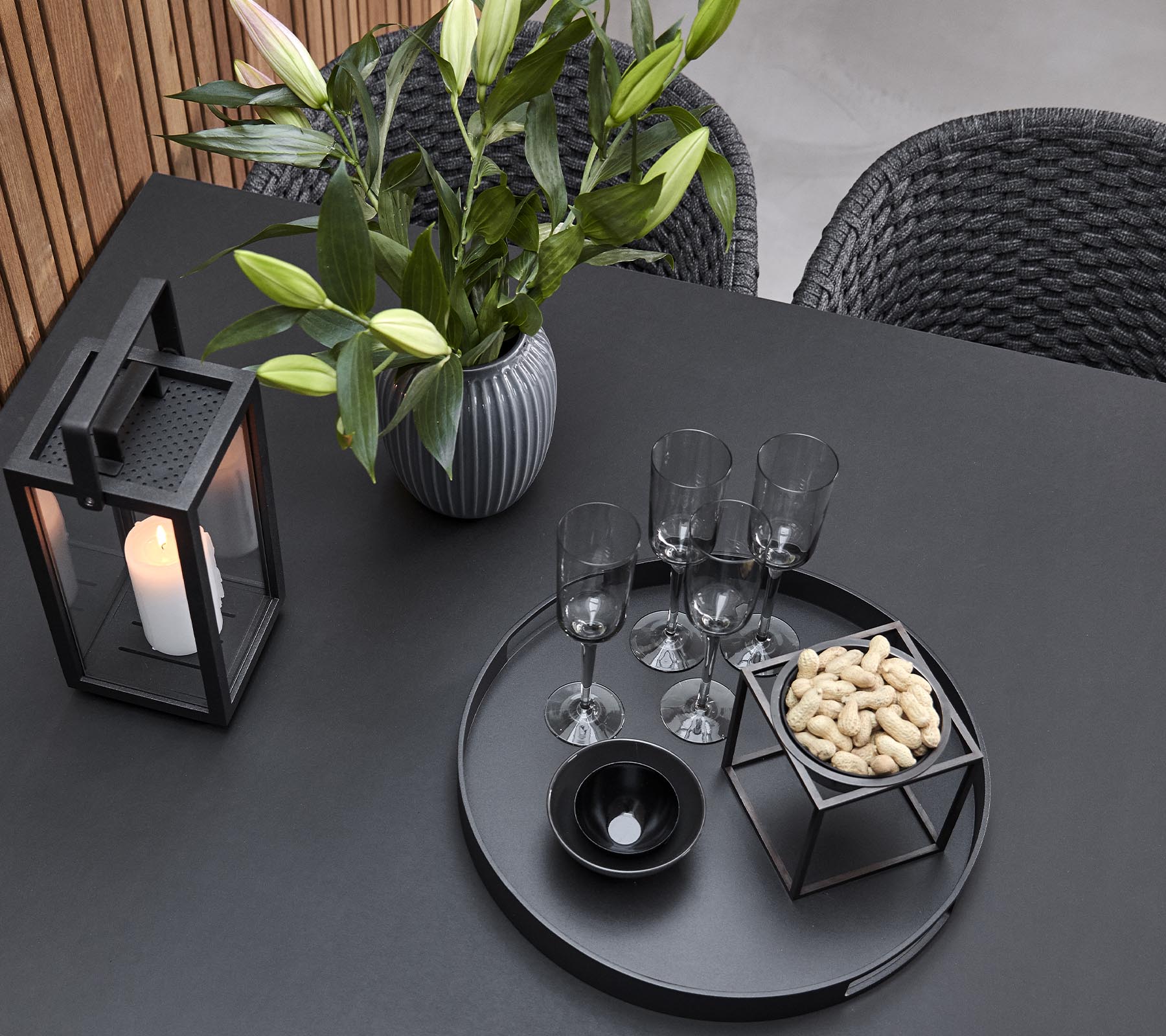 Una elegante disposición de mesa con una linterna, un jarrón con flores, copas y una bandeja de servicio con aperitivos.