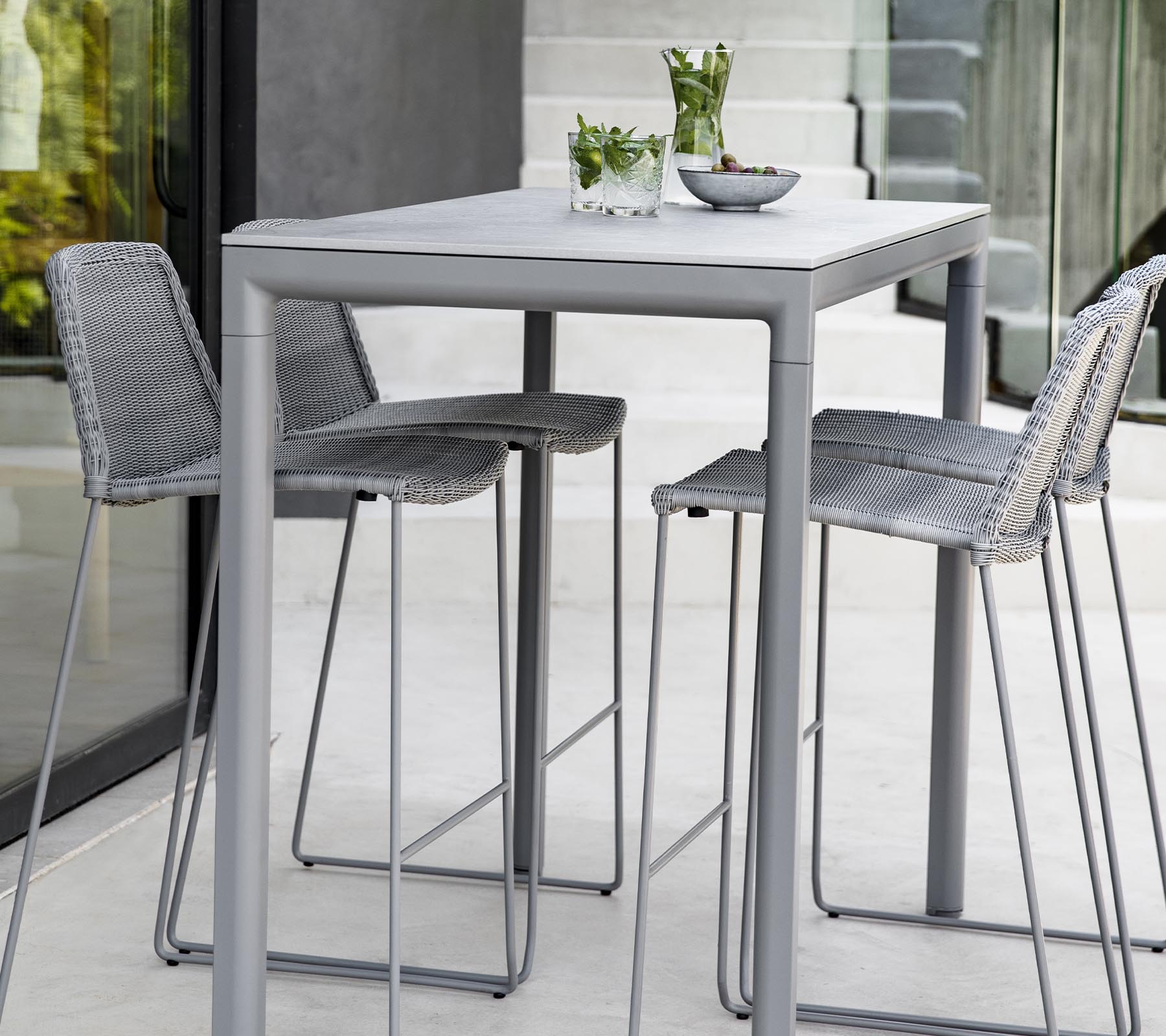 Una mesa moderna gris con tres taburetes a juego, que cuenta con plantas decorativas y un tazón en la superficie de la mesa.
