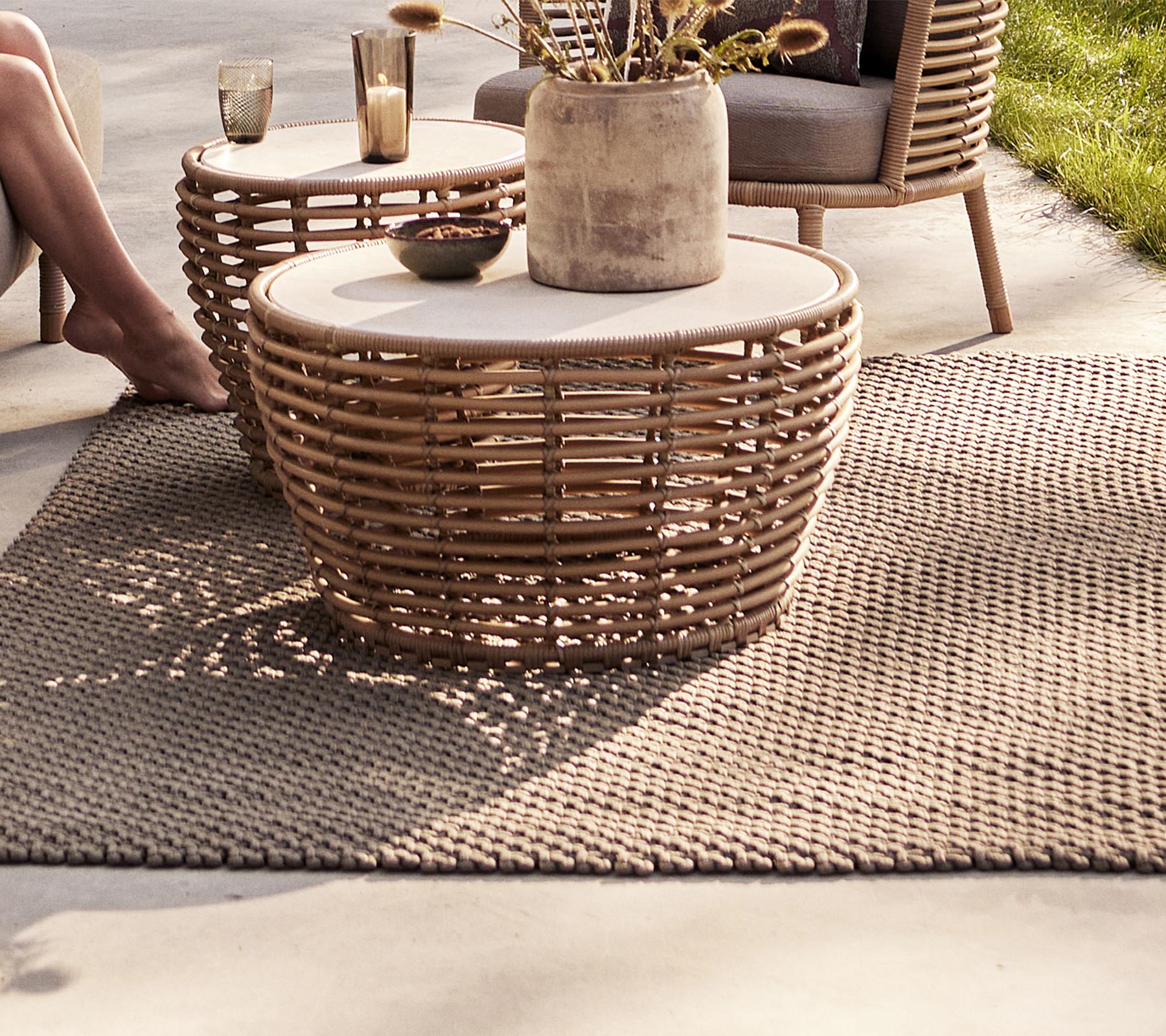 Un área de estar acogedora con mesas tejidas, un jarrón decorativo y una alfombra texturizada, perfecta para realzar un espacio elegante.