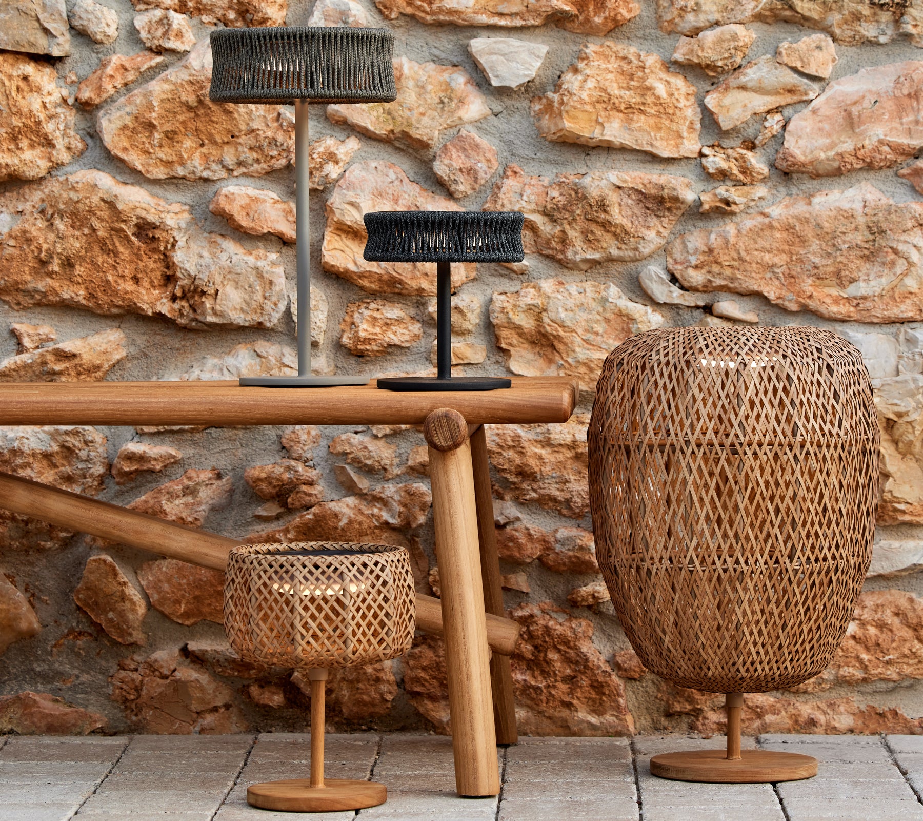 Tres lámparas decorativas de formas y tamaños variados sobre una mesa de madera, contra una pared de piedra texturizada.