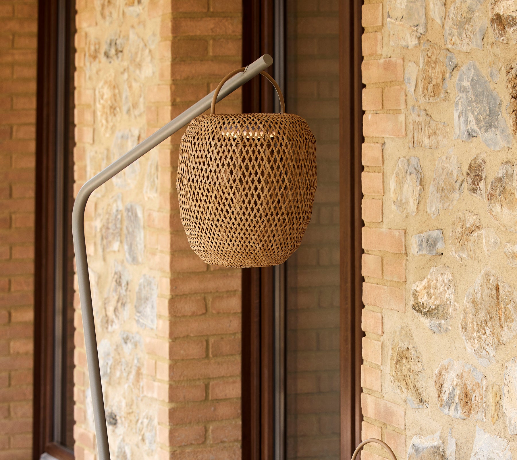 Una lámpara tejida y luminosa suspendida de un soporte elegante, que complementa una pared de piedra texturizada.