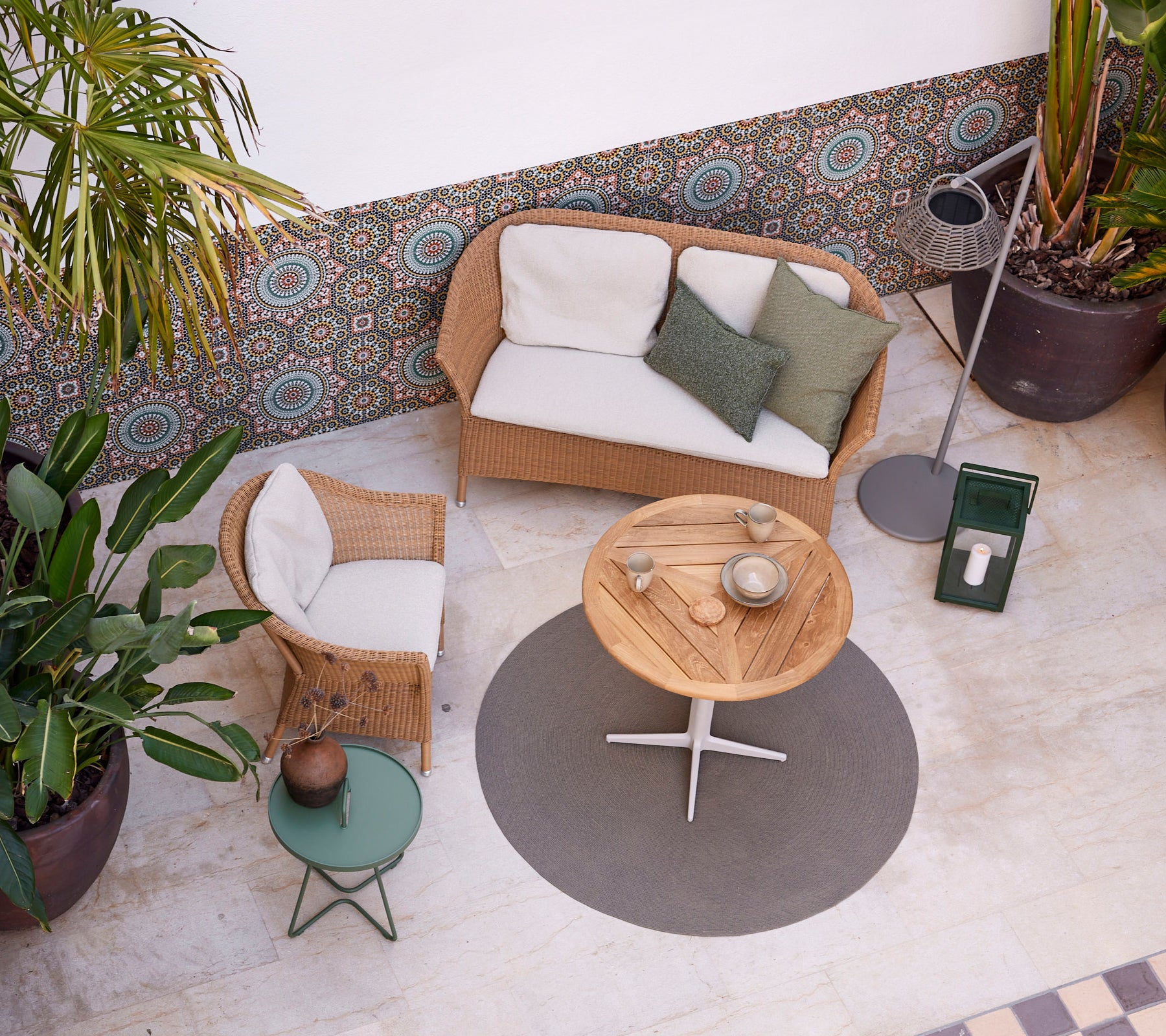 Un ambiente acogedor con un sofá y una silla Lansing, una mesa circular y vegetación, creando una atmósfera relajada. Perfecto para el ocio.