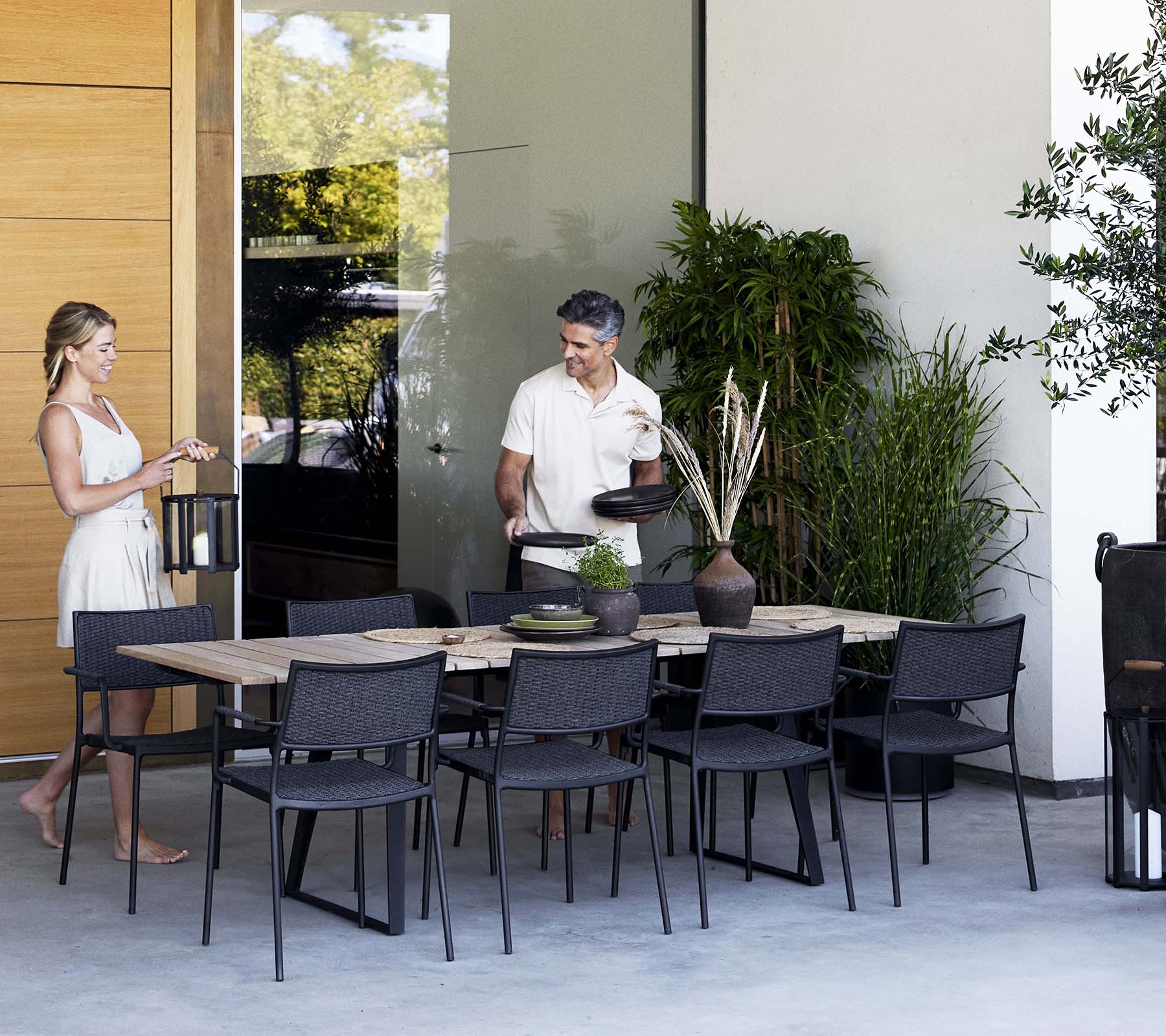 Una mujer y un hombre conversan cerca de una elegante mesa de comedor rodeada de sillas modernas y vegetación.