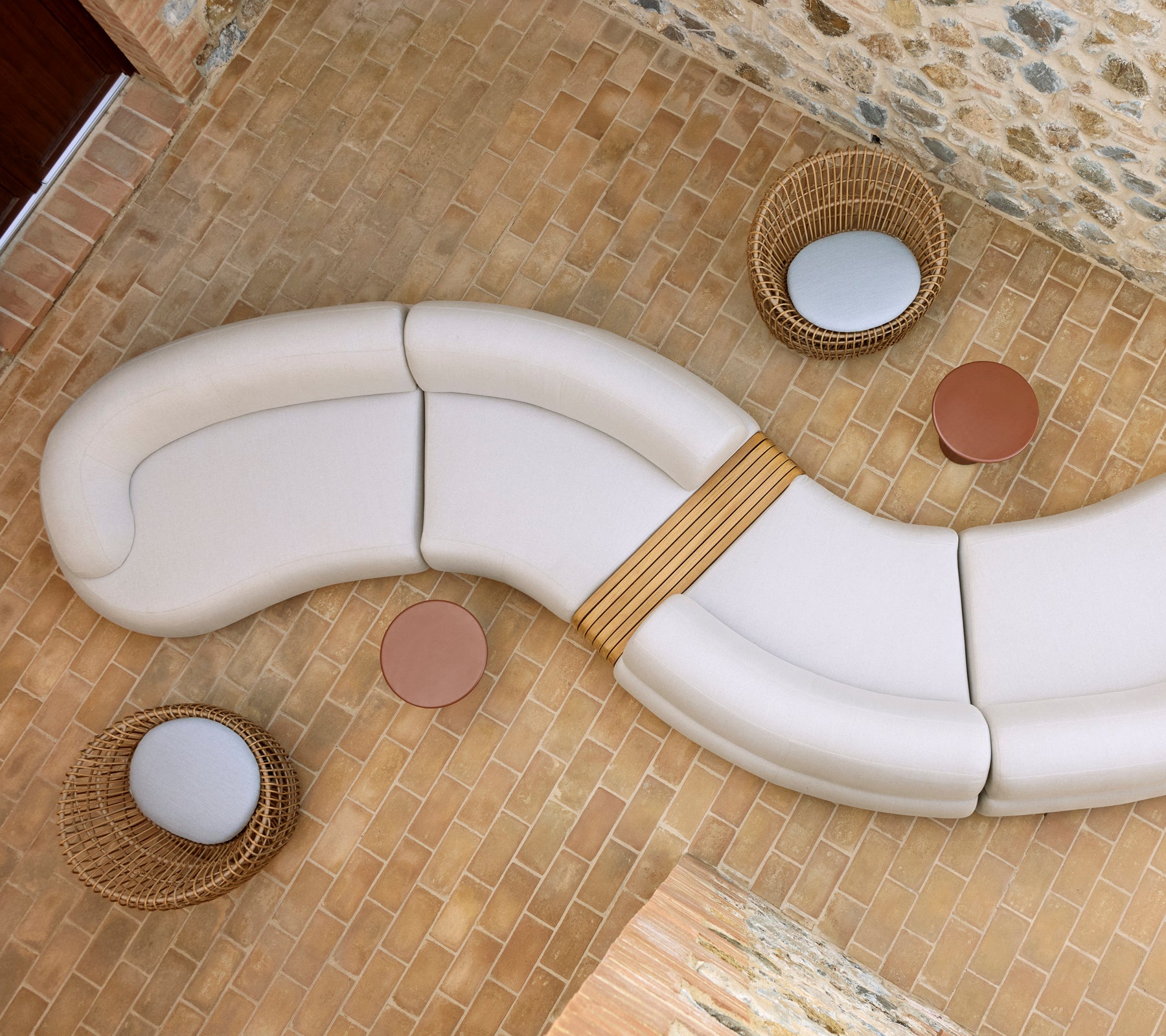 Salón tranquilo con un diseño de asientos curvado en blanco, dos mesas de café Glaze redondas y sillas Nest de mimbre en un suelo de piedra.