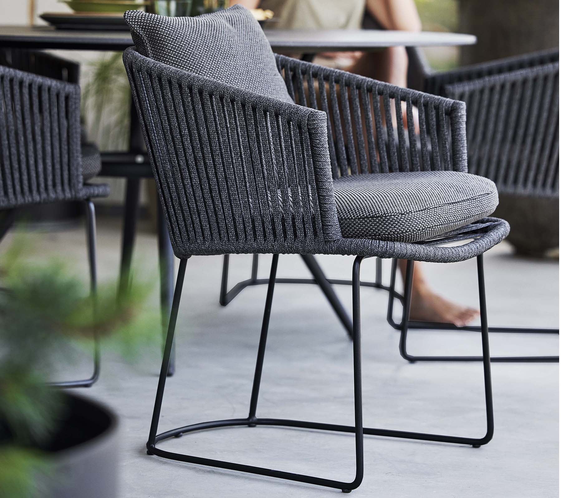 Silla elegante con un diseño trenzado y un cojín suave, apoyada en un marco de metal refinado, perfecta para espacios contemporáneos.