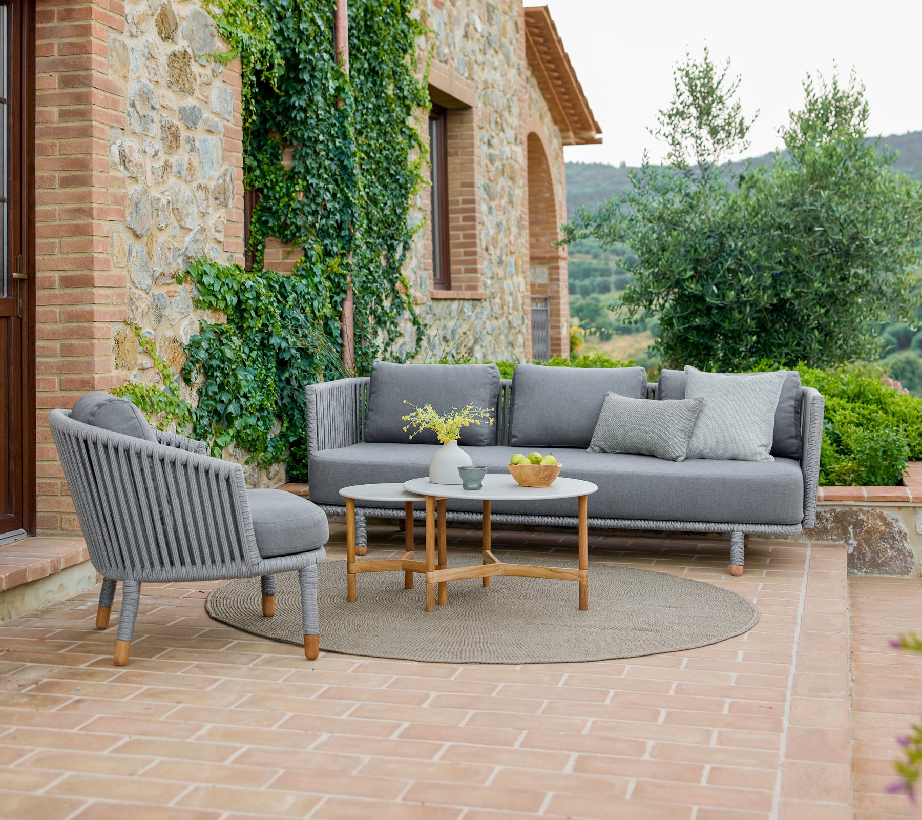 Sillón y sofá elegantes con una disposición acogedora, acompañados de mesas de café elegantes, rodeados de vegetación.