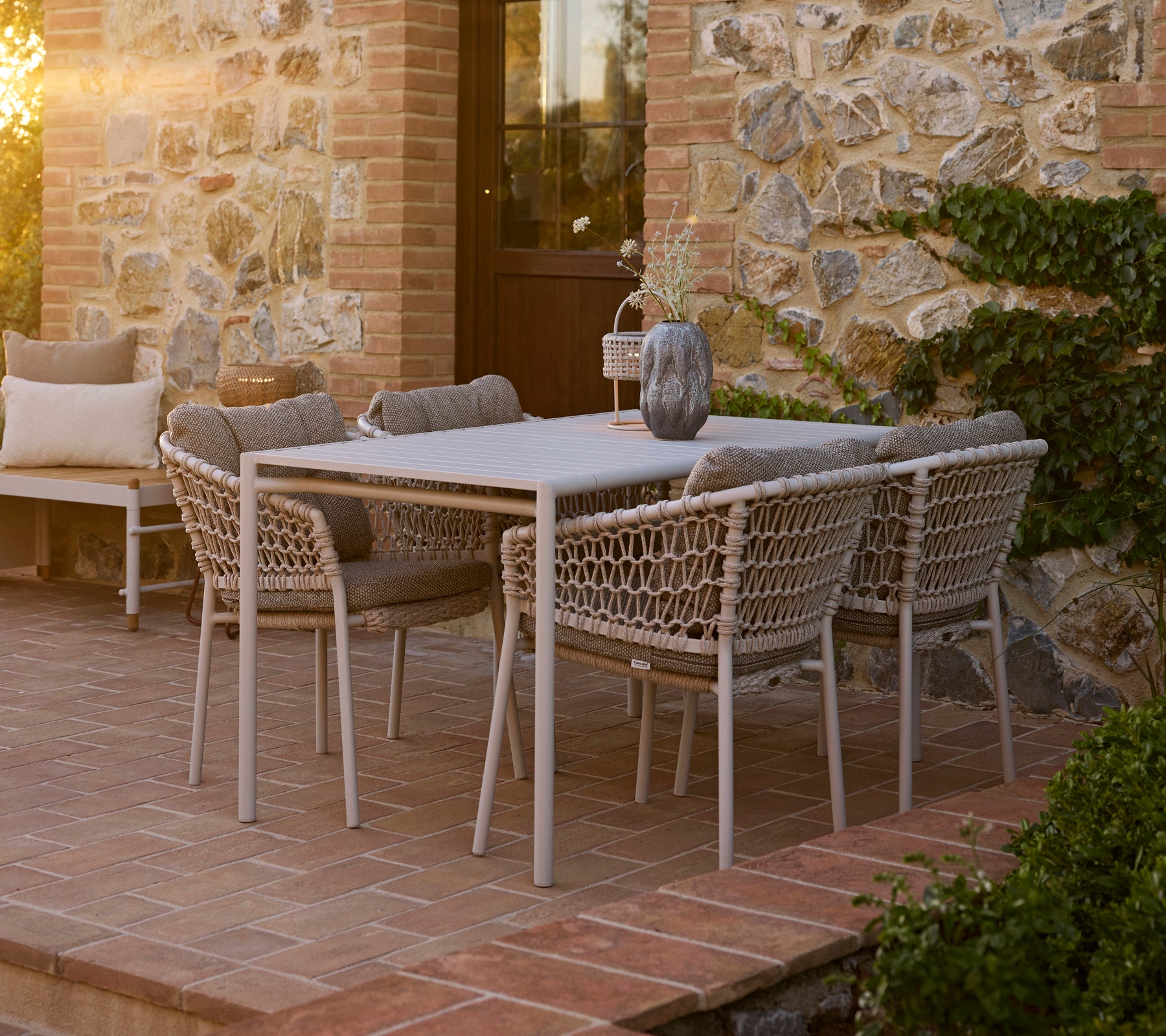 Configuración de comedor playera con una mesa Bliss rodeada de sillas de comedor Ocean, con un encantador fondo de piedra.
