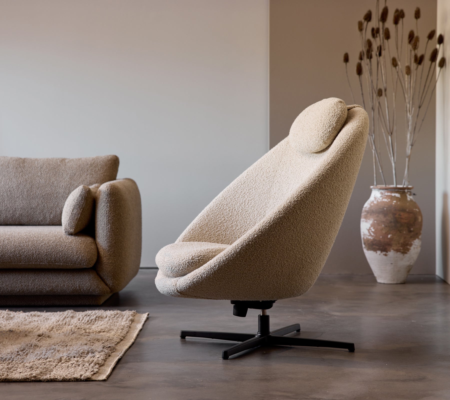 Silla Pace de tela taupe junto a un sofá Bloom de 3 plazas, complementada con un jarrón decorativo y una sutil textura del suelo.