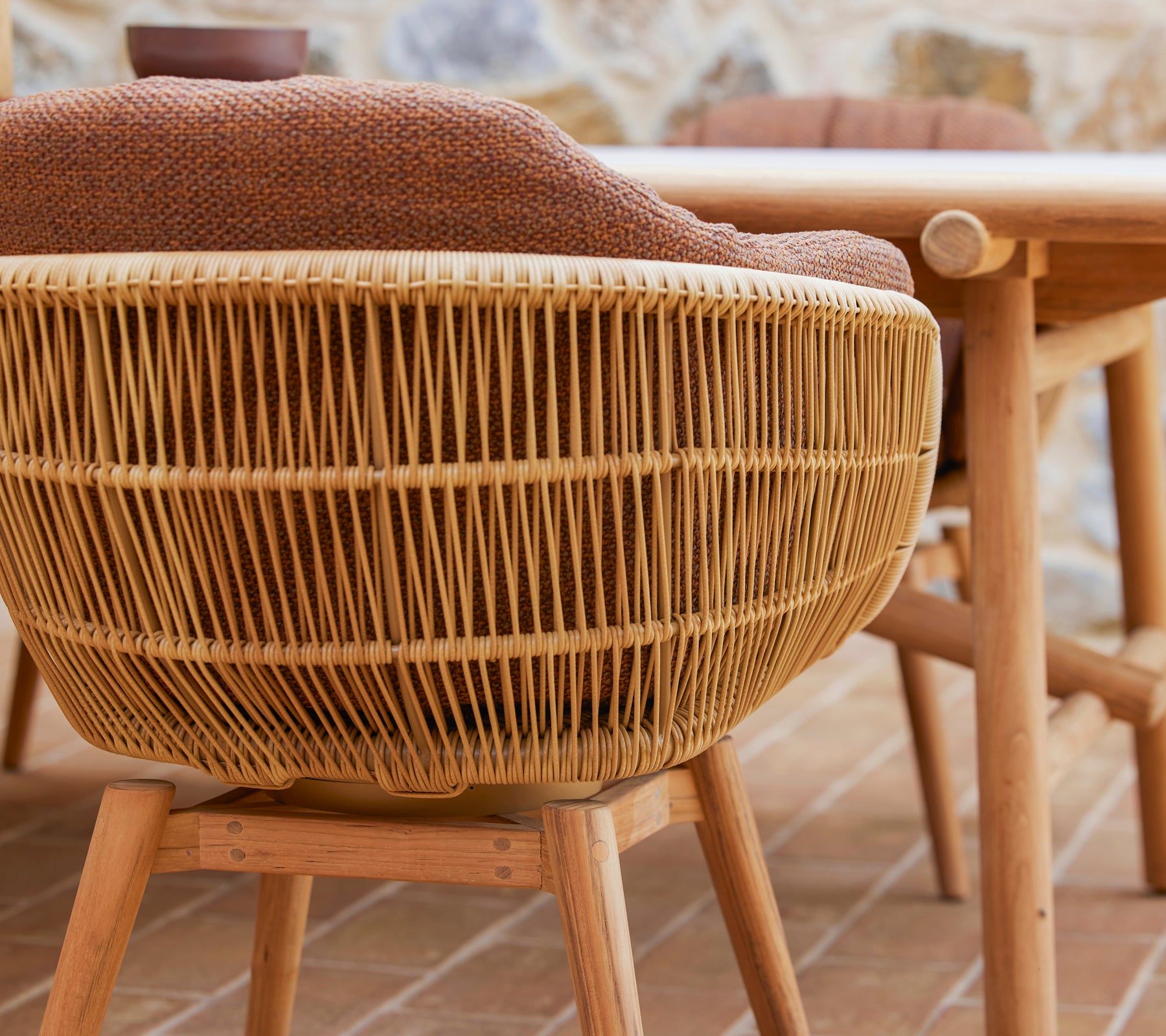 Silla de comedor giratoria con un diseño tejido y patas de teca, que cuenta con un cómodo cojín Rice para mayor estilo y confort.