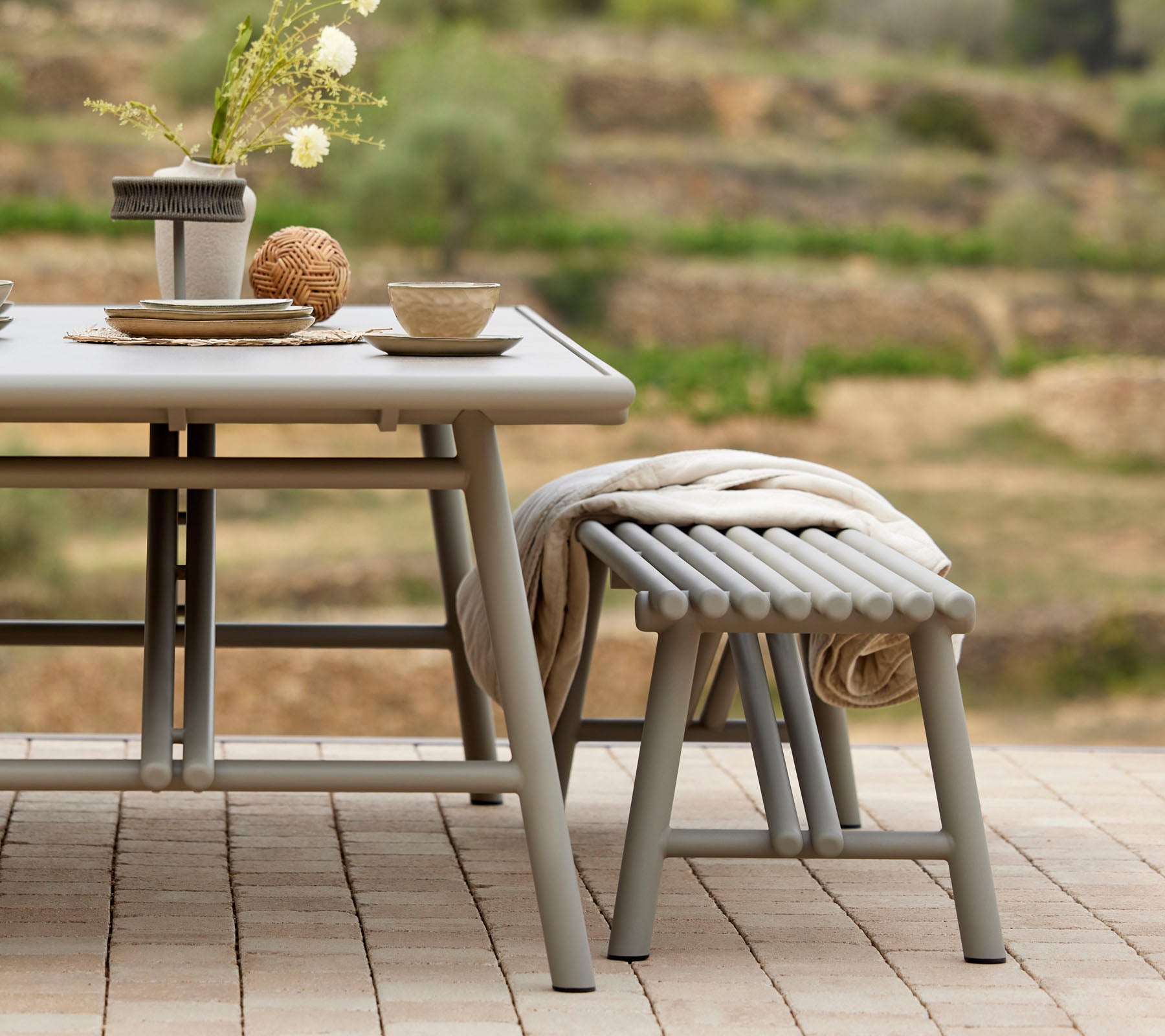Una elegante decoración de mesa con cuencos, tazas y un centro decorativo, acompañado de un taburete de estilo palo a juego.
