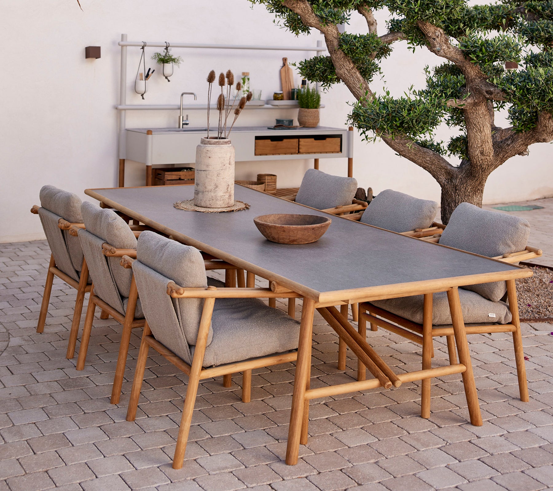 Mesa de comedor de teca rodeada de sillas cómodas, con elementos naturales y un estilo decorativo minimalista.