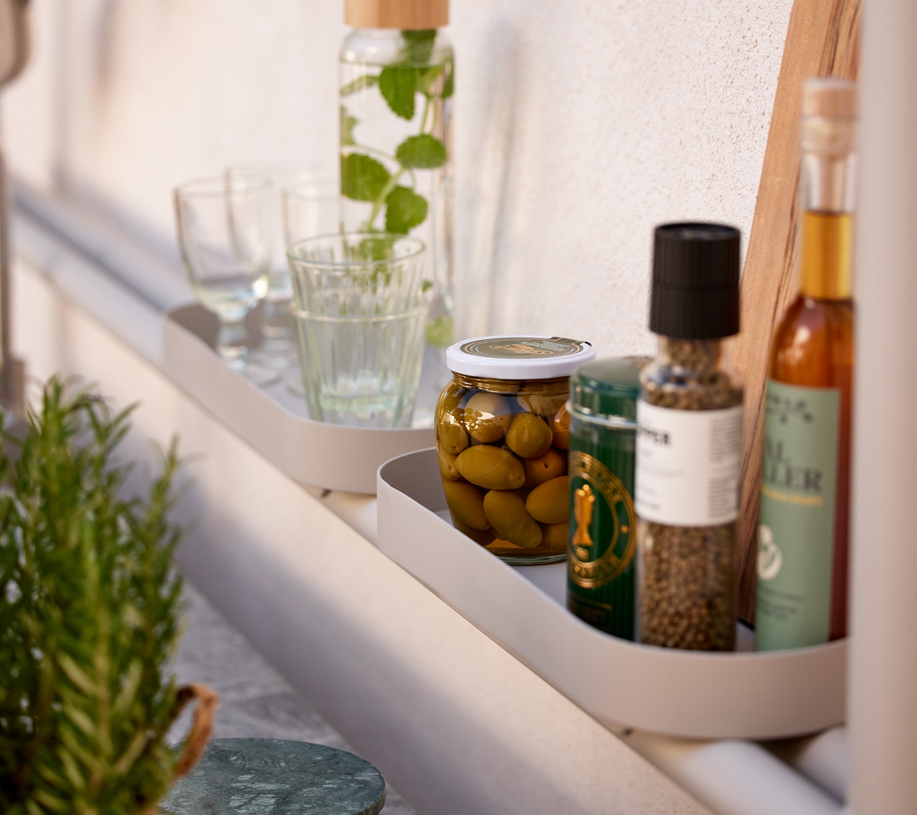 Una estantería que exhibe varios artículos de cocina, incluyendo vasos, tarros de aceitunas y botellas de aceite y especias.