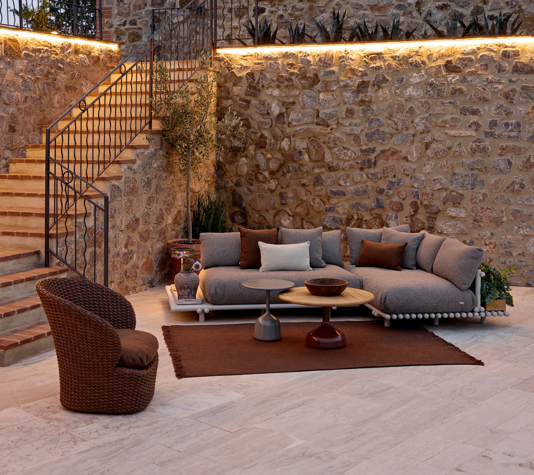 Área de estar acogedora con un sofá modular con cojines, una mesa de café redonda, una alfombra de punto y una silla de lounge tejida.
