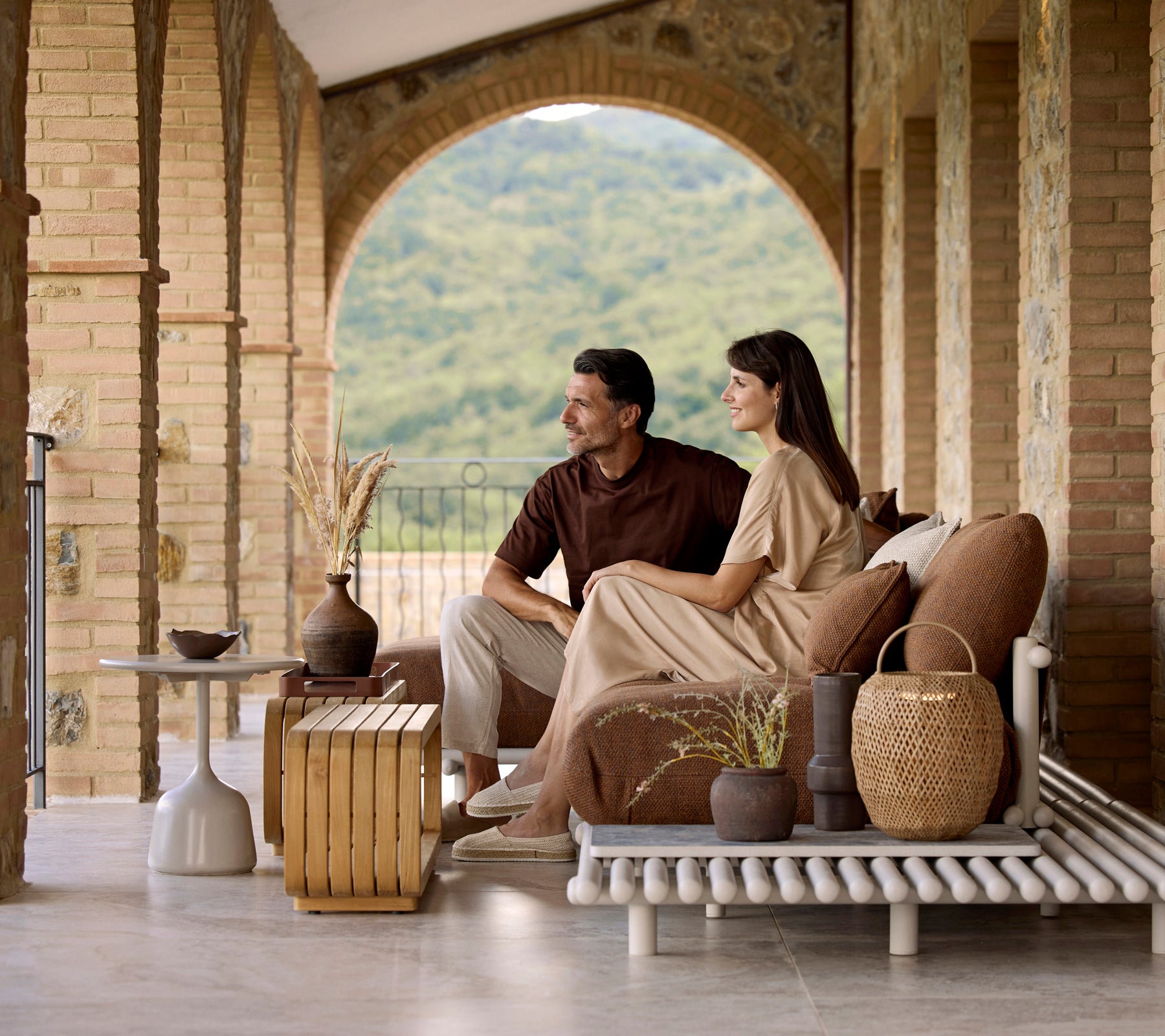 Una pareja sentada en un sofá elegante, disfrutando de una mesa de café Mellow con elementos decorativos y una vista serena de fondo.