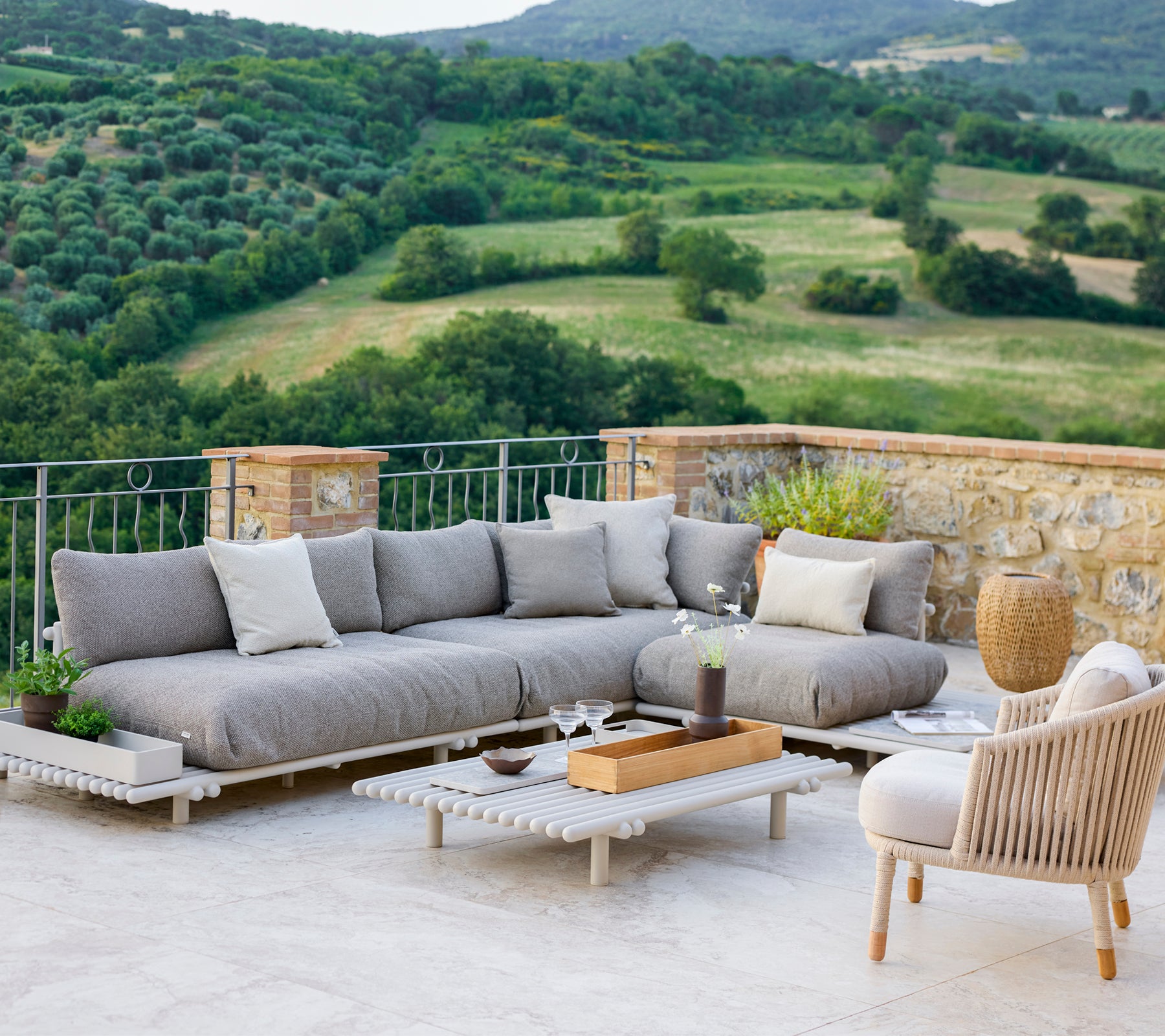Área de lounge elegante con un sofá seccional gris y una silla cómoda, ubicada frente a un paisaje escénico.