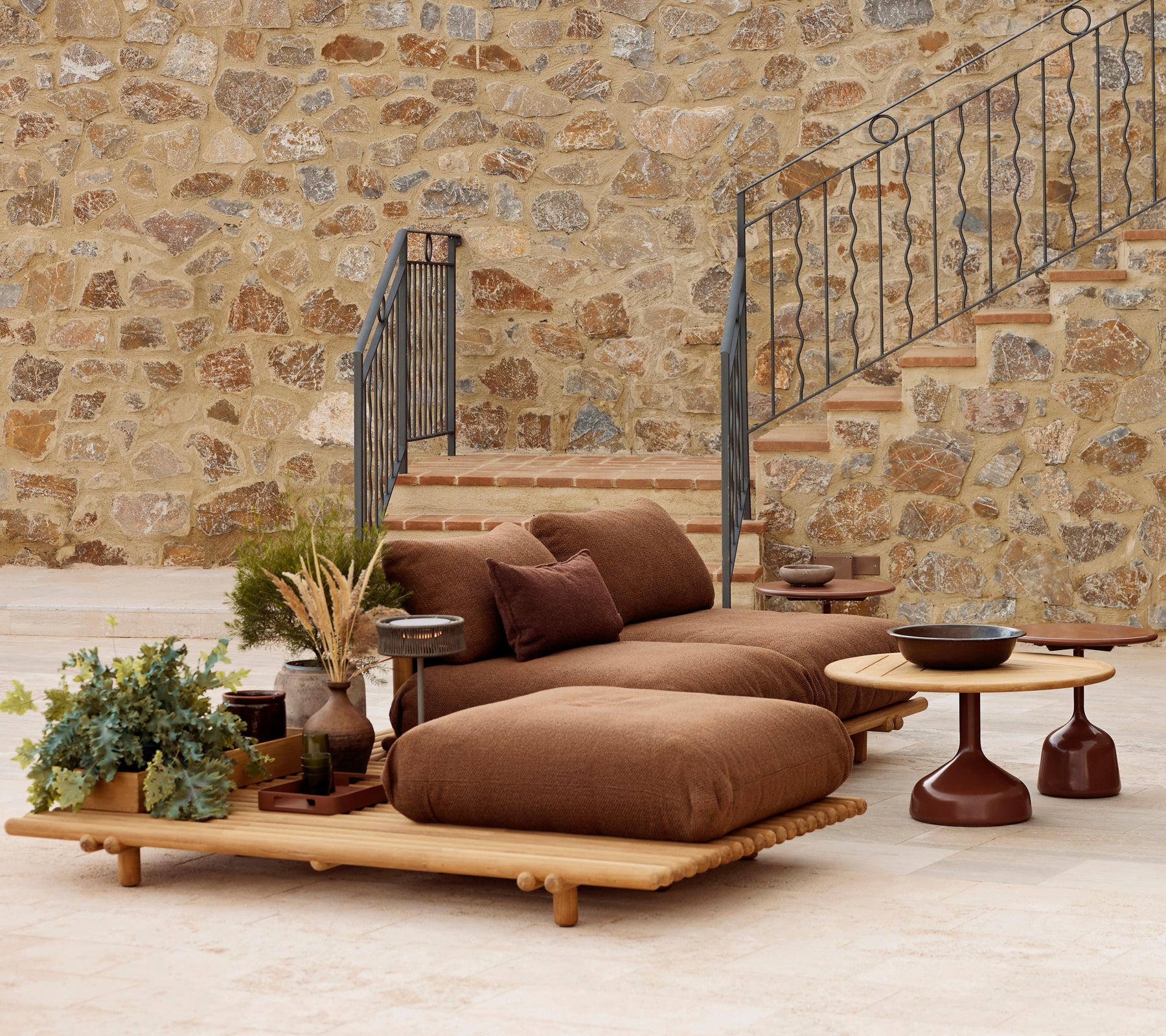 Sala de teca con cojines suaves y una mesa de café Glaze, complementada con plantas decorativas y un fondo de piedra texturizada.