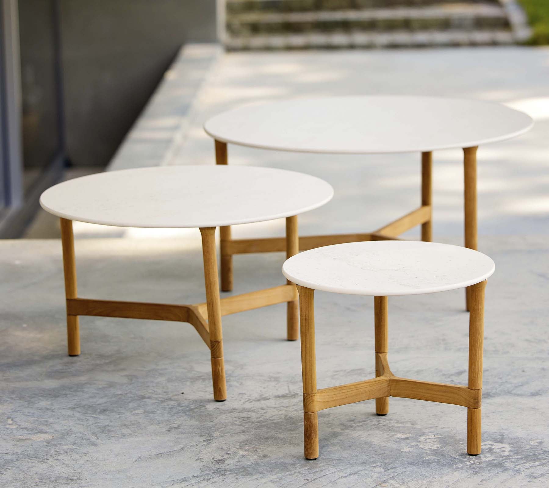 Tres mesas de café modernas de diferentes tamaños con tapas blancas y patas de madera, que muestran un diseño elegante y minimalista.