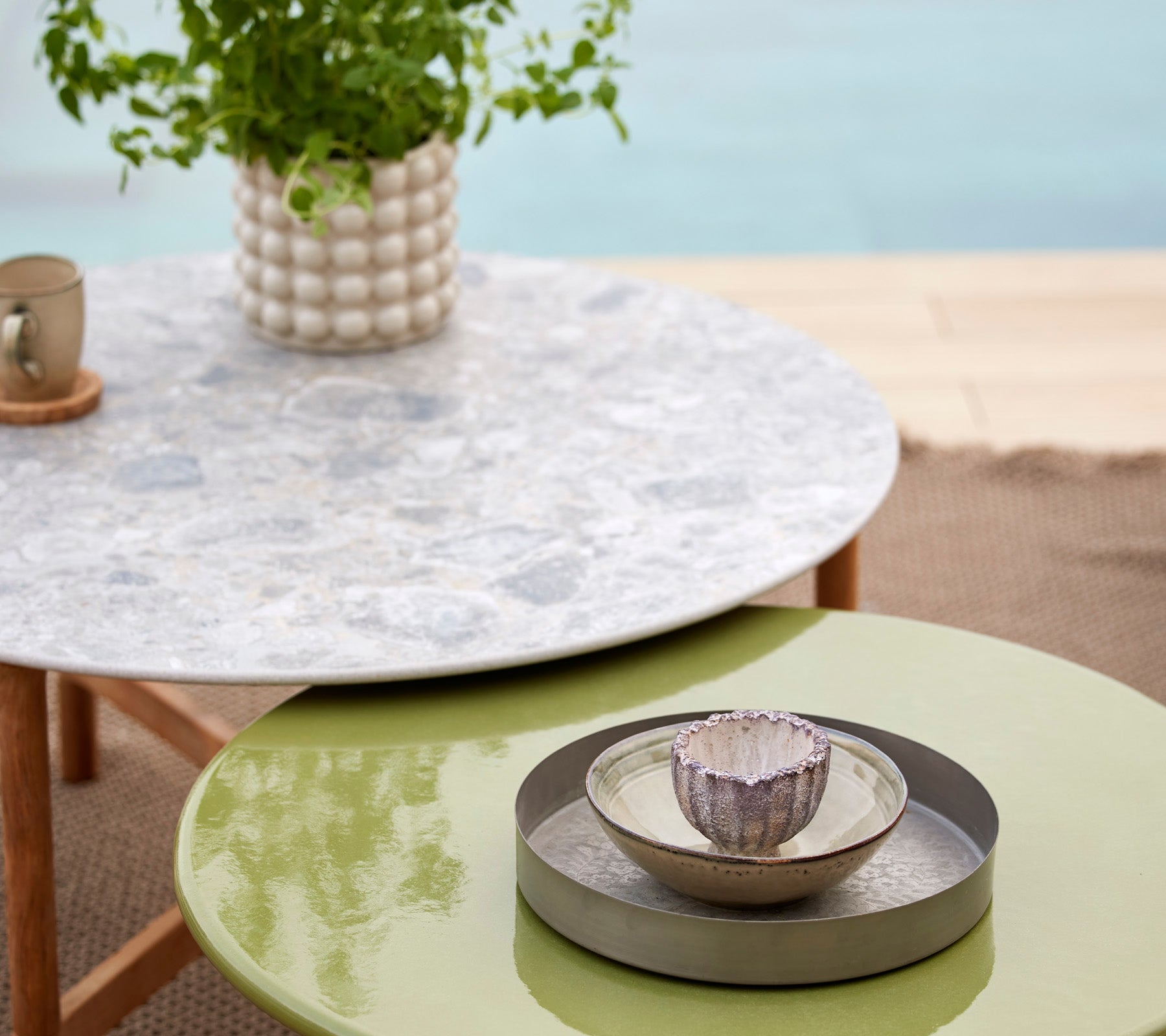 Una mesa Twist multicolor con una tapa de piedra de lava esmaltada, acompañada de un cuenco decorativo y una planta en un entorno elegante.