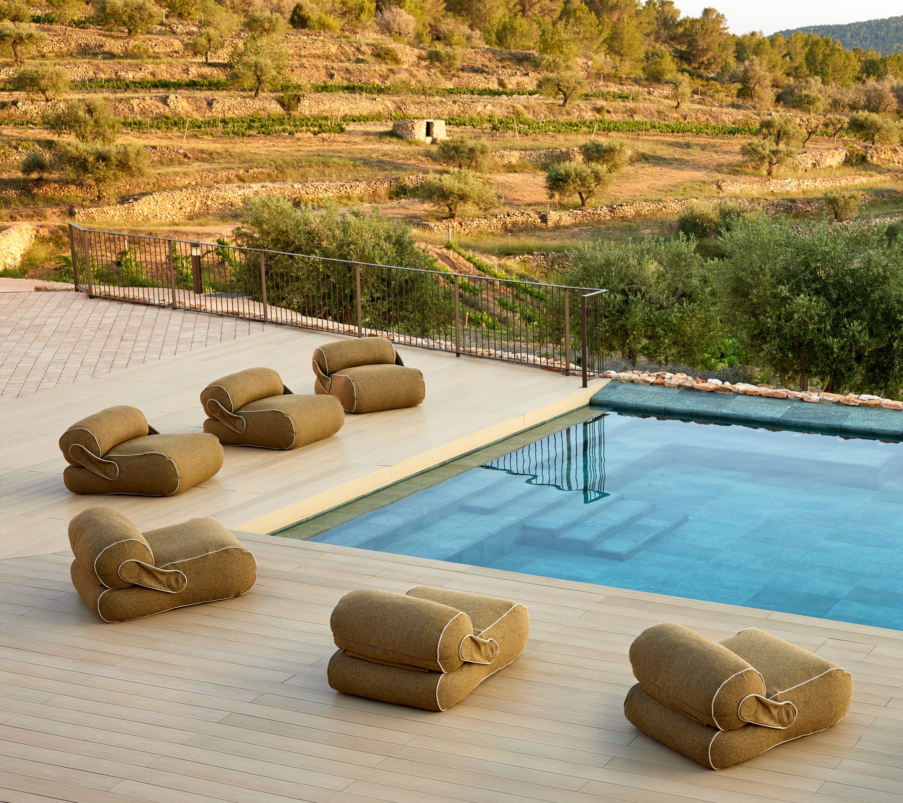 Un entorno sereno con asientos de salón acolchados dispuestos cerca de una piscina tranquila, rodeada de exuberante vegetación y un paisaje pintoresco.