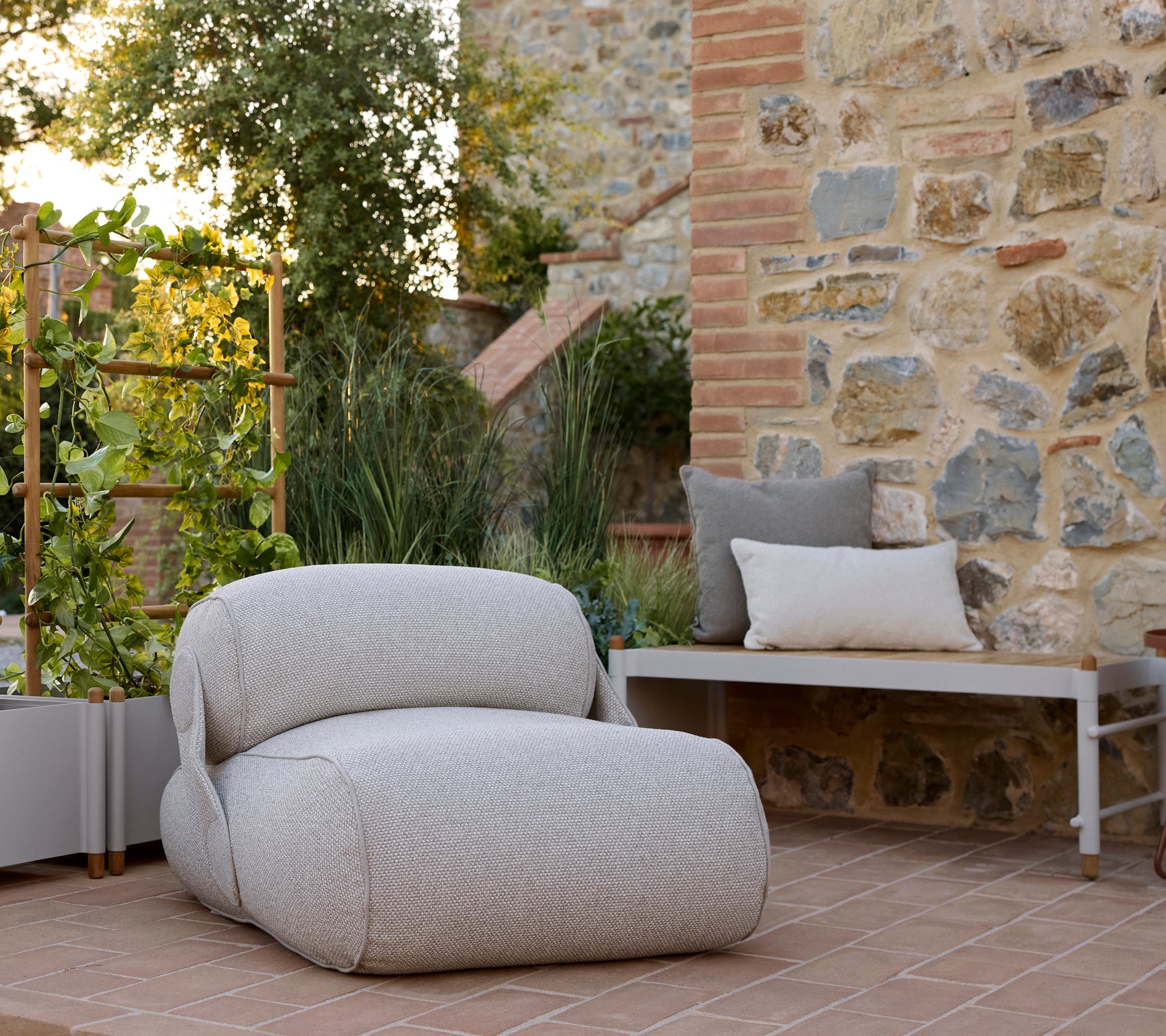 Una silla de lounge acogedora con una tela texturizada, acompañada de un banco de planta elegante y abundante vegetación en un entorno sereno.