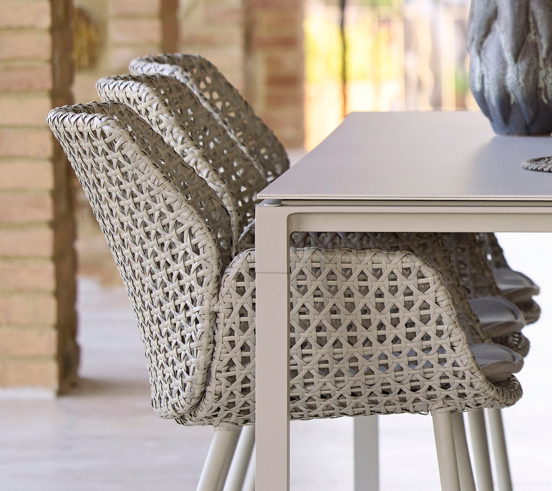 Sillas apiladas con un diseño tejido único al lado de una mesa de comedor lisa y minimalista, creando una disposición de comedor moderna y acogedora.