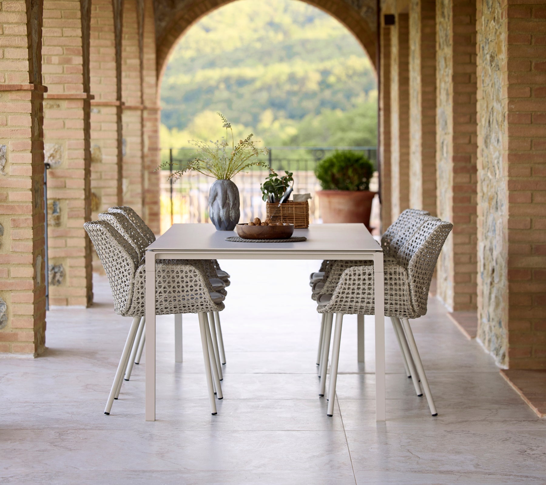 Configuración de cena elegante con una mesa de comedor Pure sand rodeada de sillas de comedor Vibe, acentuada por un jarrón y elementos decorativos.