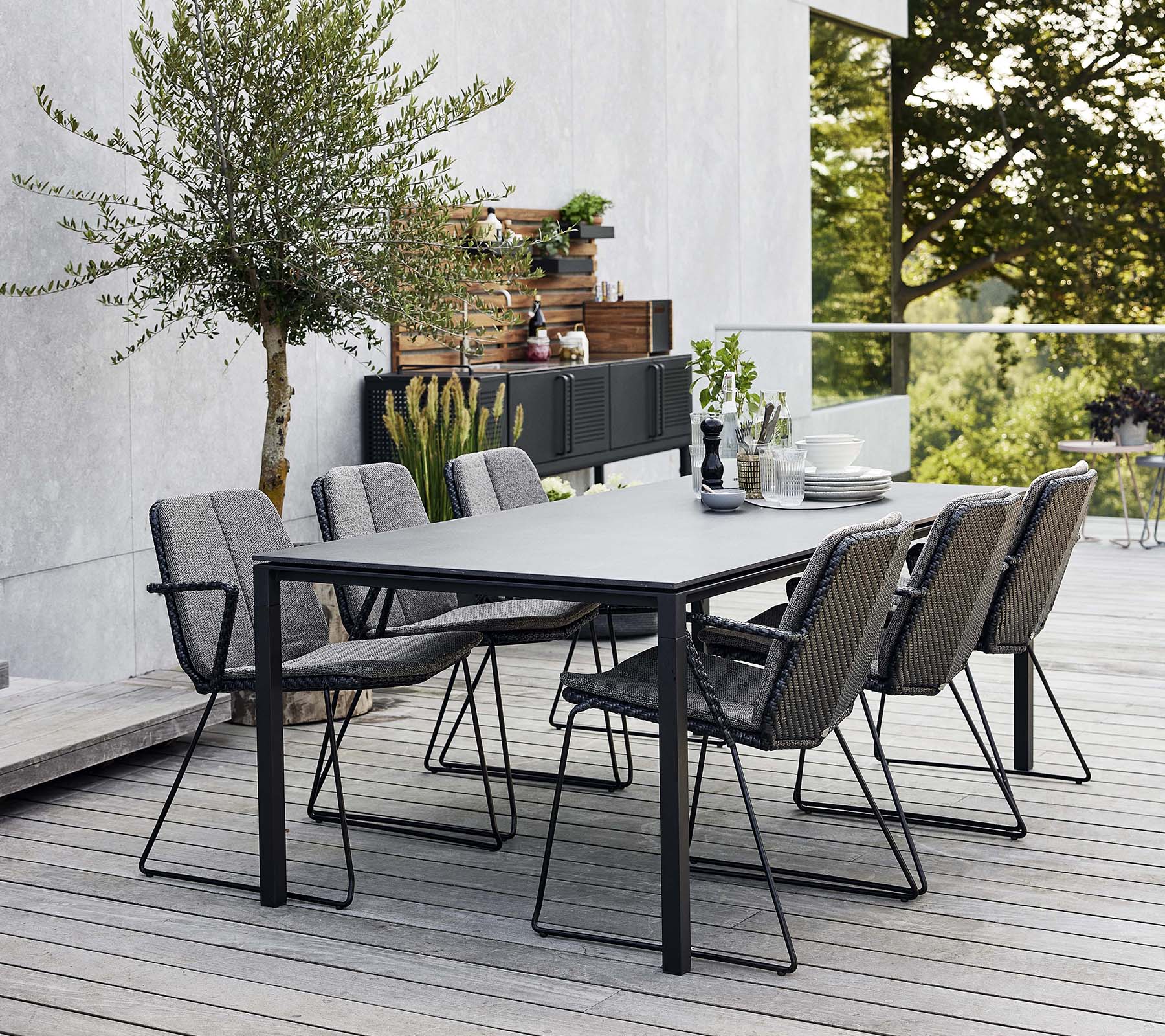 Un elegante conjunto de comedor al aire libre con una mesa estilizada y varias sillas cómodas, rodeado de vegetación y un fondo moderno.